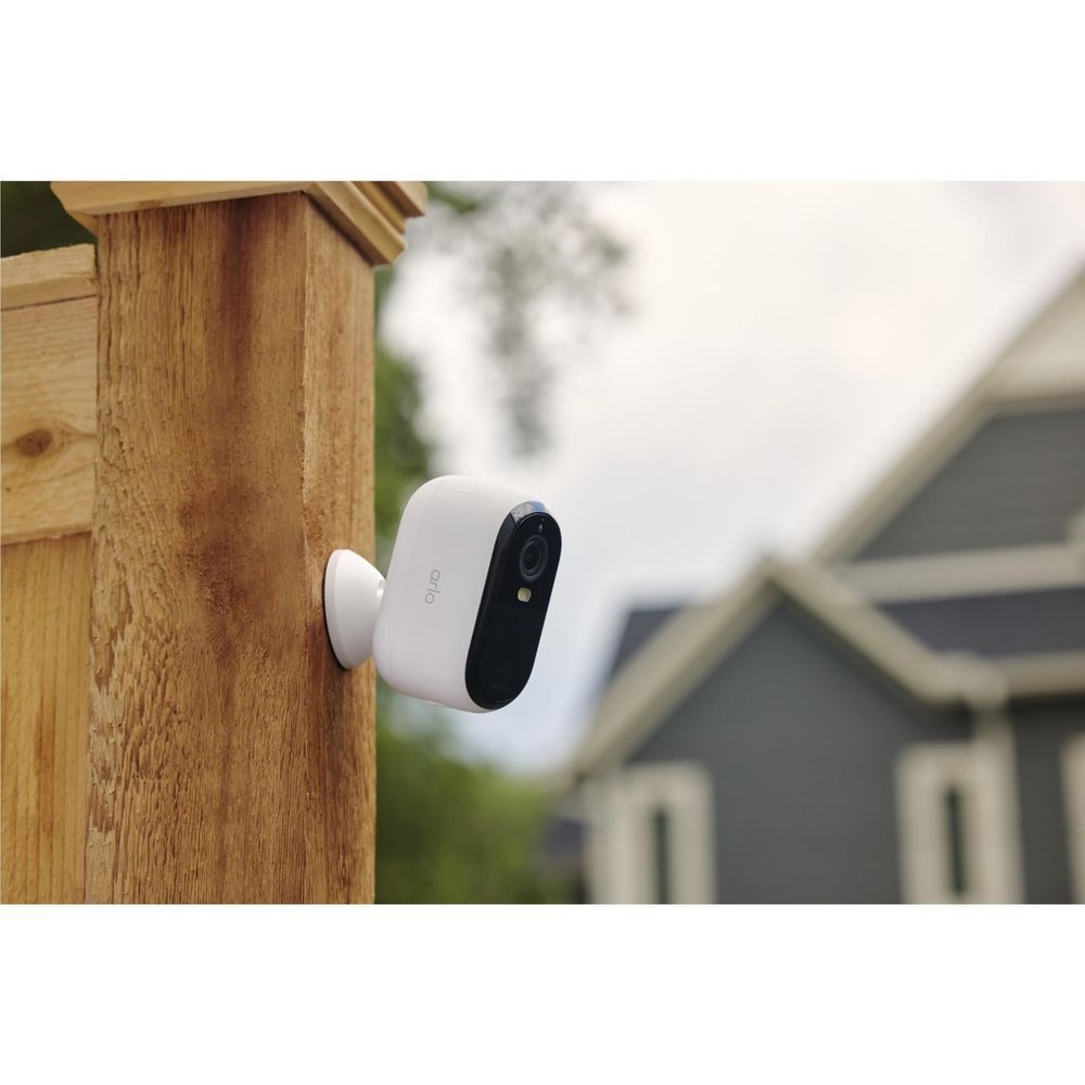 White outdoor security camera with lens facing wood fence on home exterior