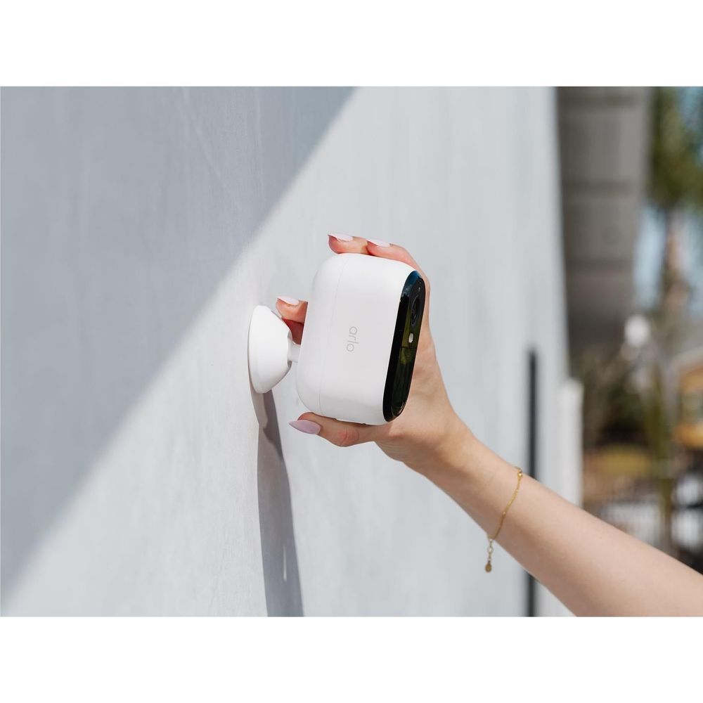 Outdoor security camera held by hand against a light wall with lens and indicator visible