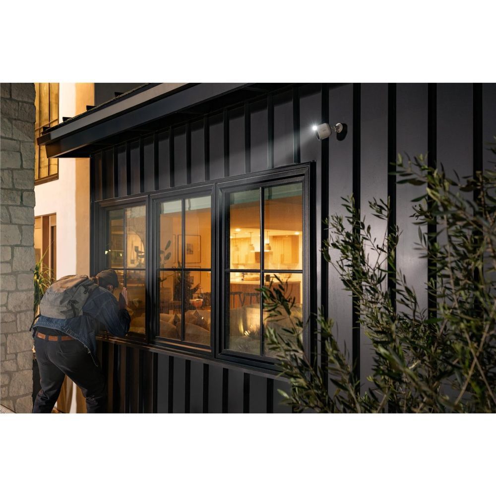 Outdoor security camera with white body mounted near a window on exterior wall