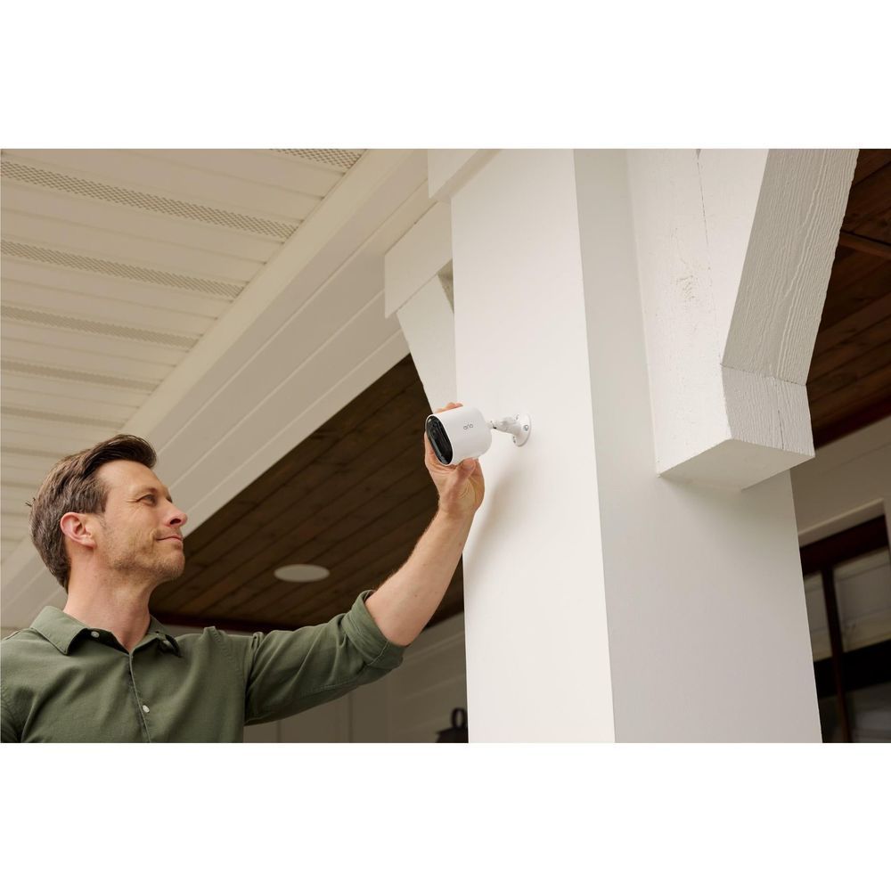 White Arlo security camera mounted near ceiling with viewing lens facing out