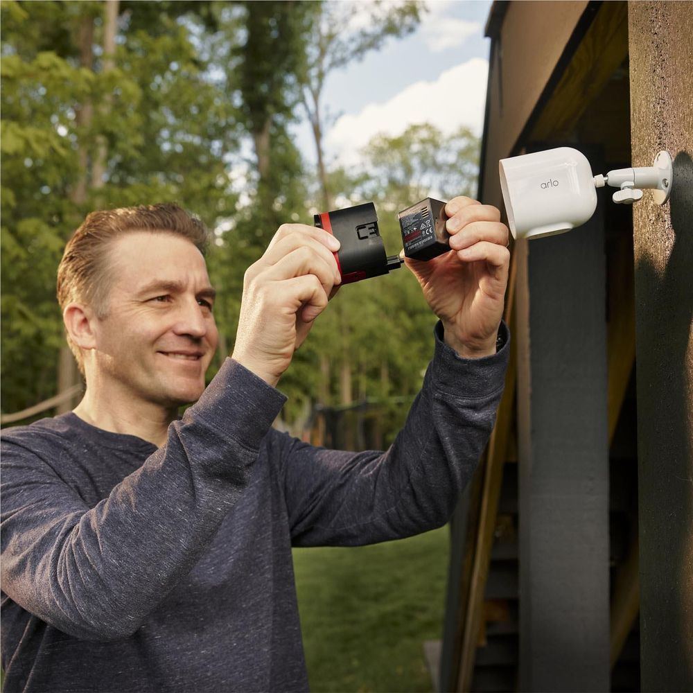 White outdoor security camera on a post while a person holds a memory card
