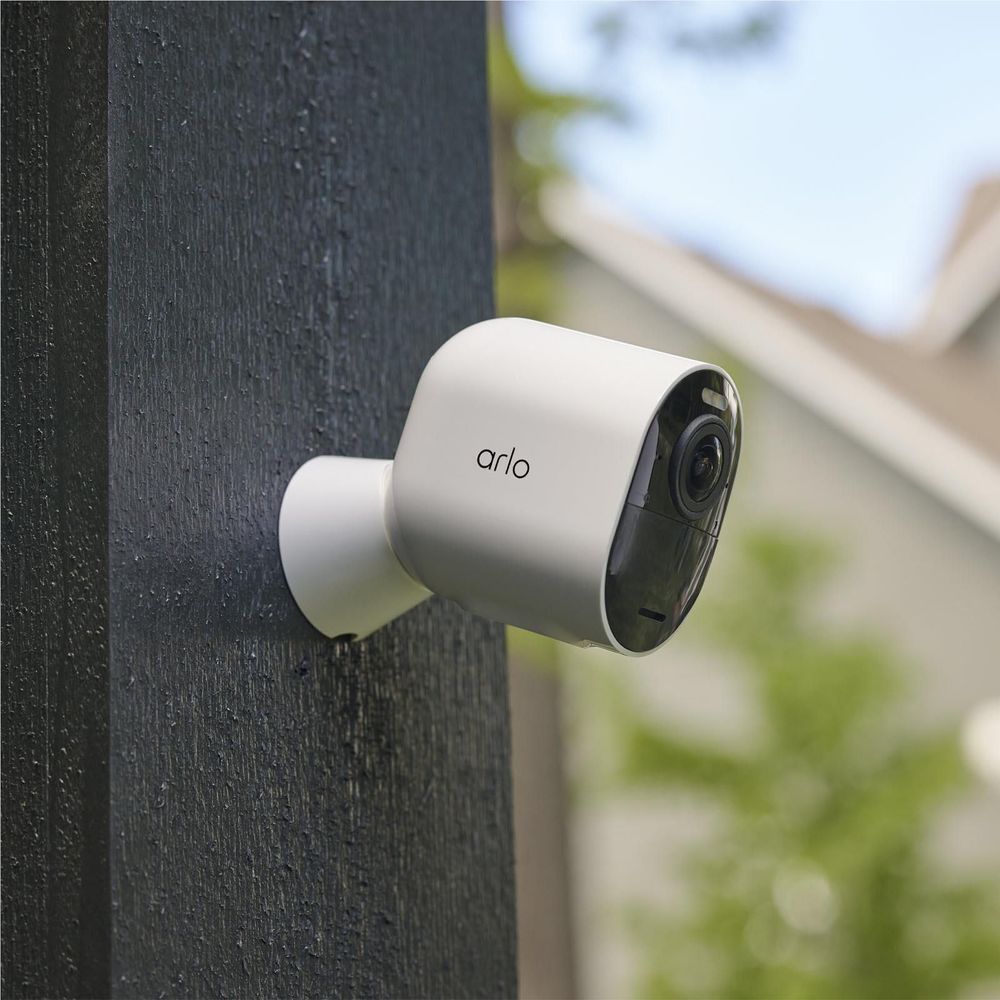 White outdoor security camera mounted on a dark wall with visible lens and black trim