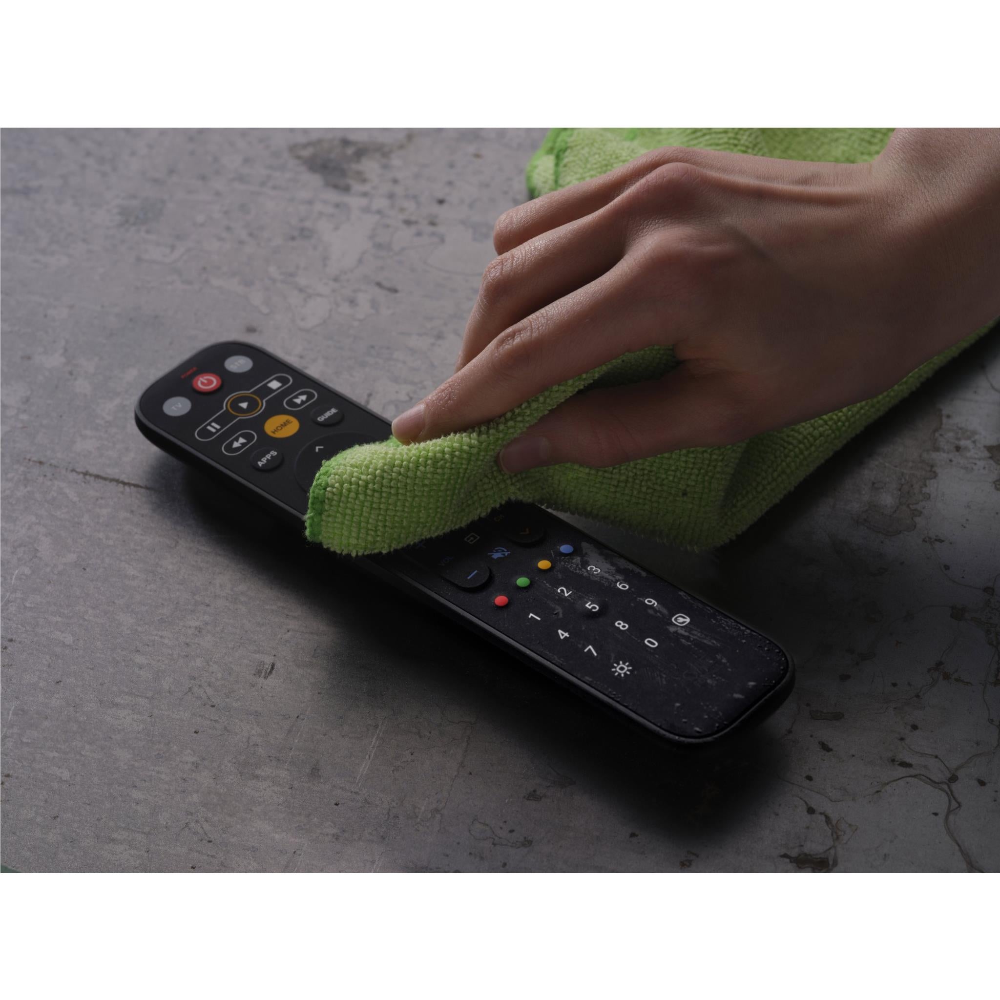Universal TV remote being cleaned with a green microfiber cloth wiping the keypad.