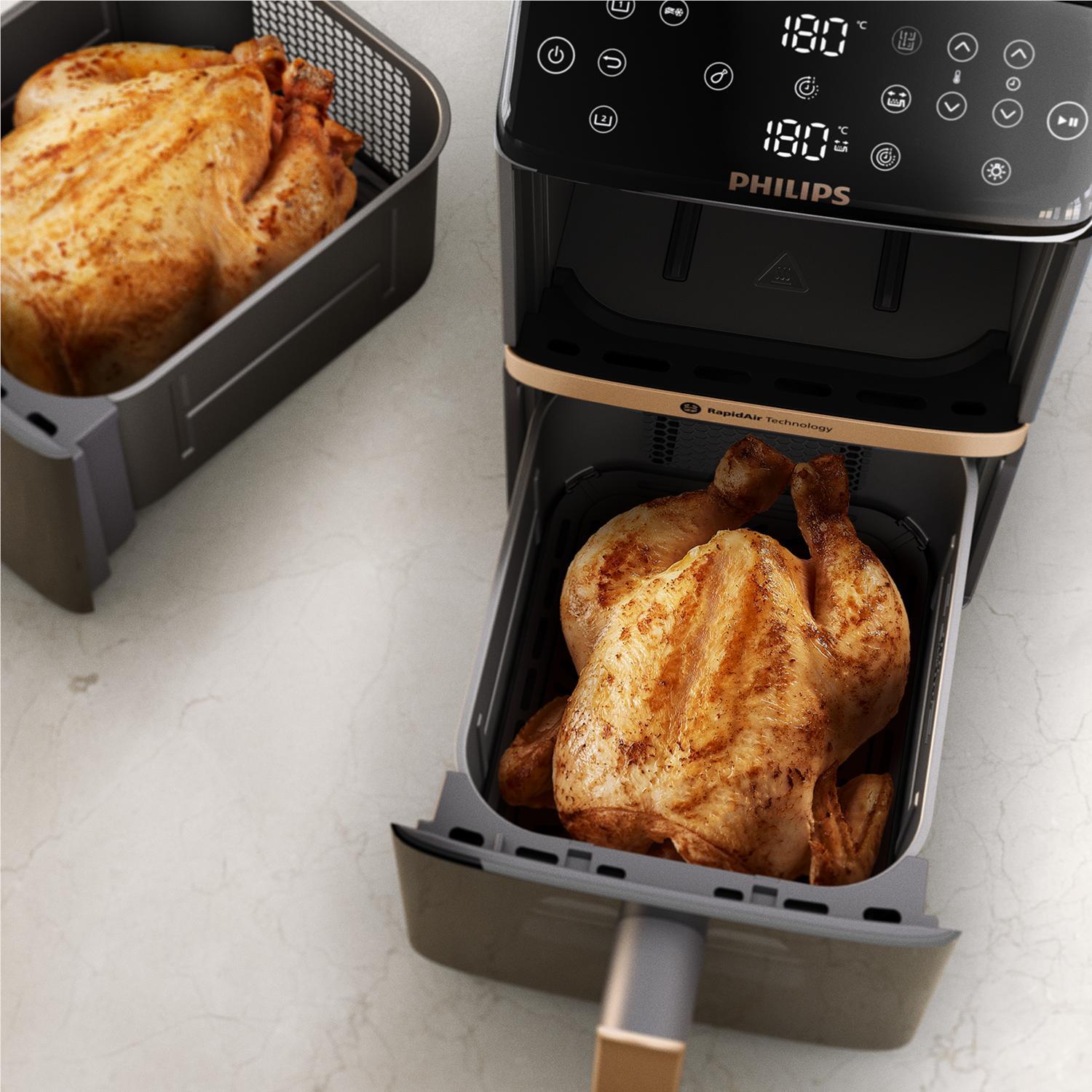 Dual-basket air fryer with cooked chicken in lower basket, black unit and handles.