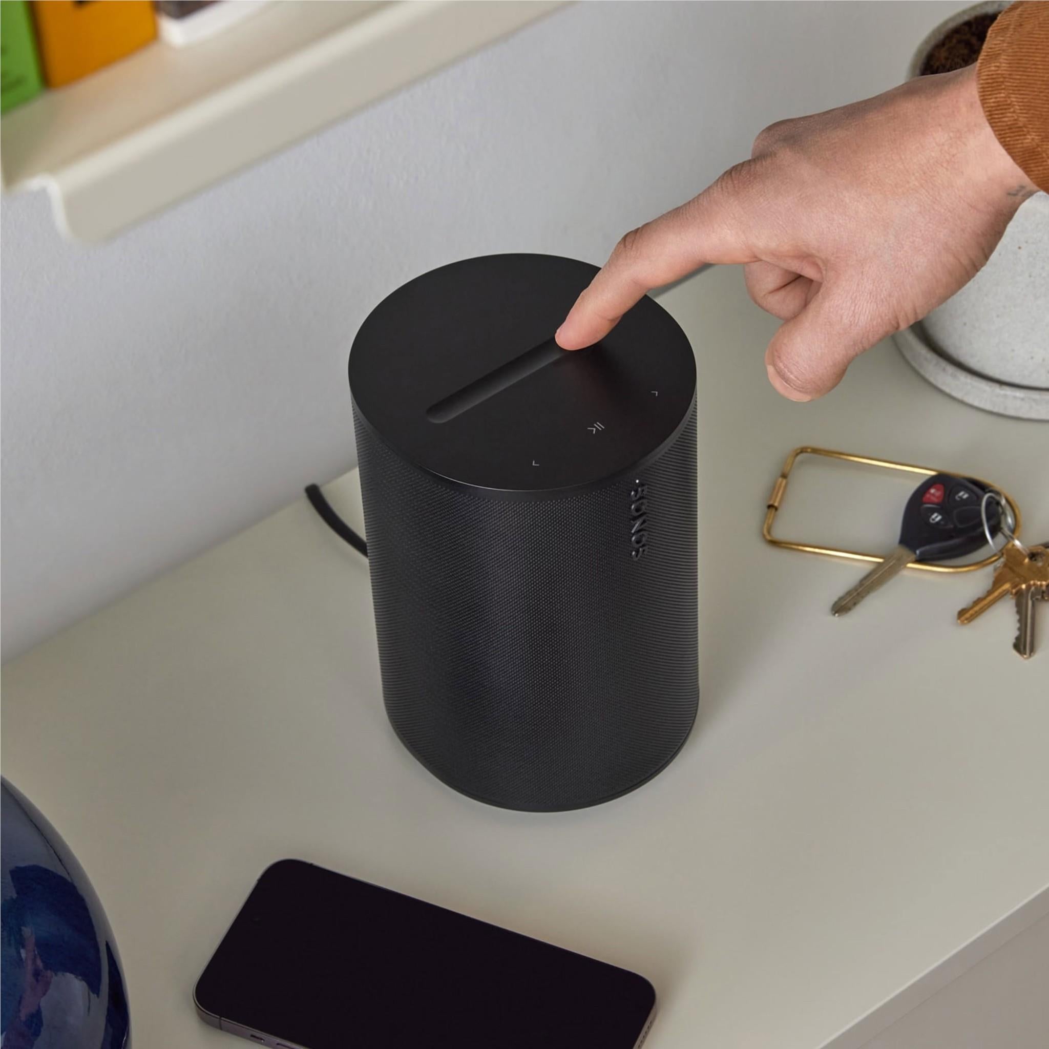 Black Sonos smart home speaker on a desk as a hand reaches the top controls