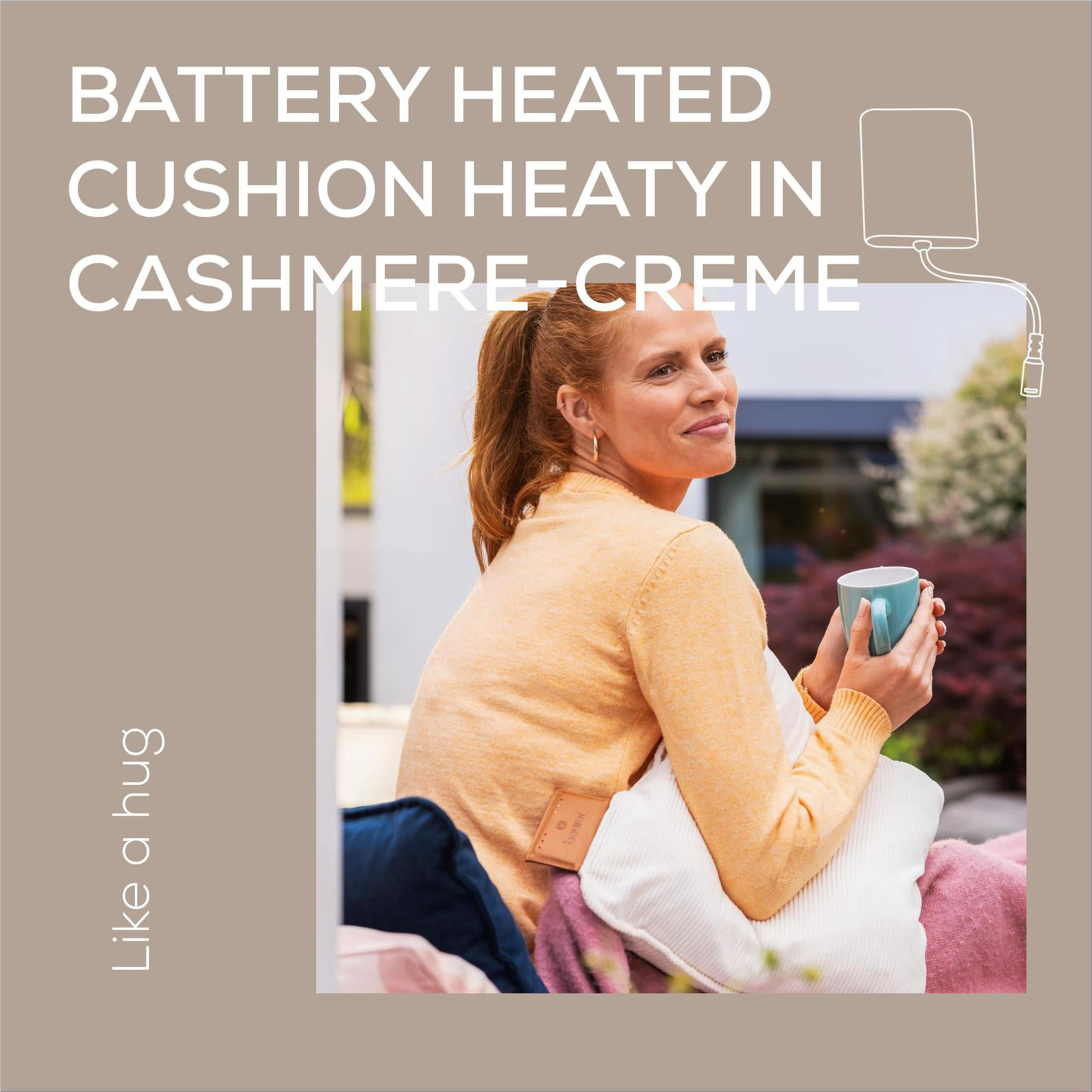 Light cream heated cushion shown beside a seated person holding a cup.