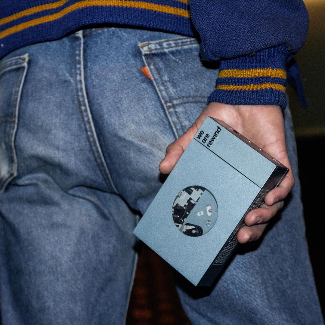 Close-up of hands holding a blue rechargeable Bluetooth cassette player with circular window