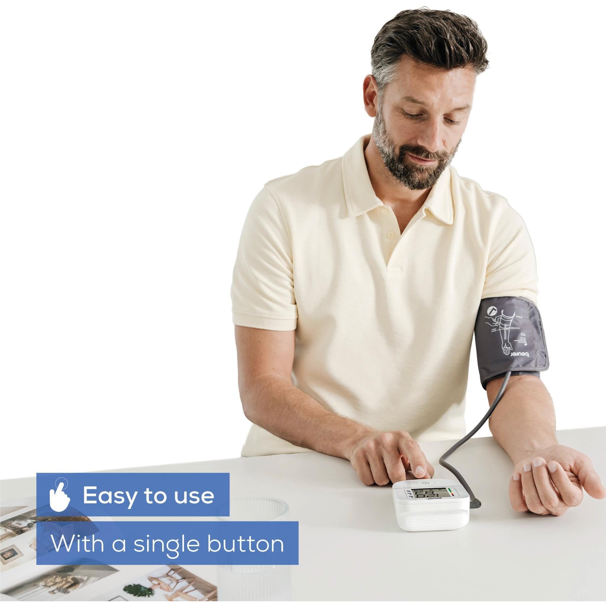 Upper arm blood pressure monitor cuff on man's arm with white monitor unit on table