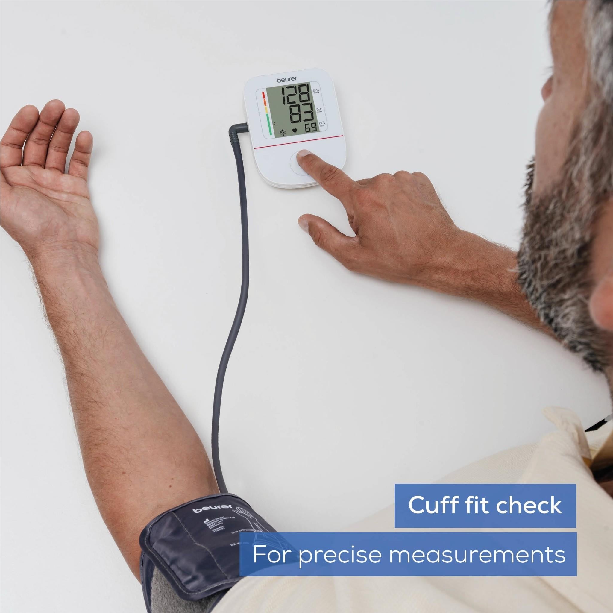 Upper arm blood pressure monitor cuff on arm with hand pressing white monitor screen