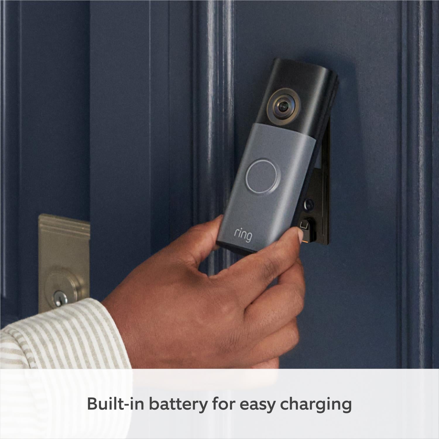Battery video doorbell held near a door frame, with black camera lens and blue ring