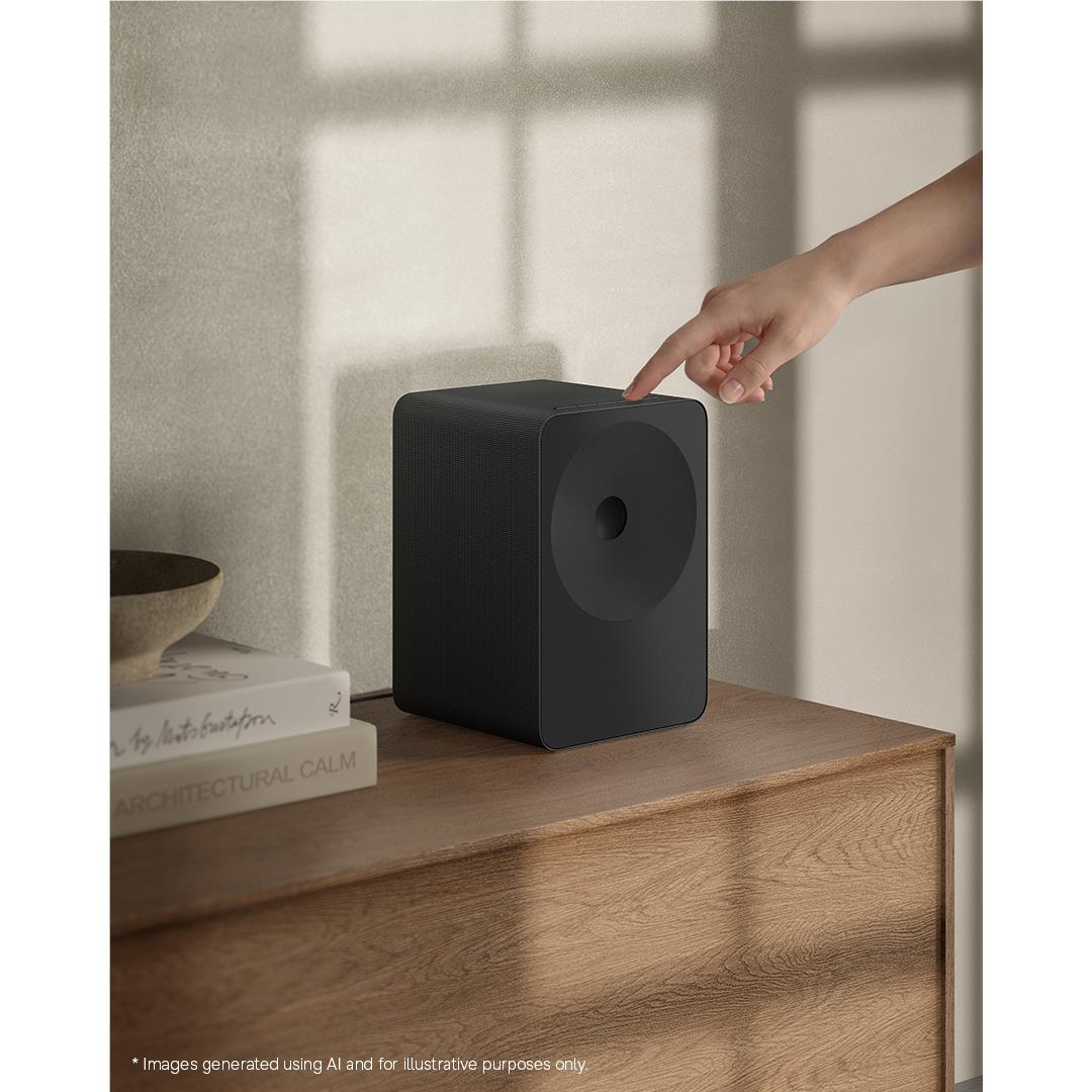 Black Wi-Fi Atmos speaker on a shelf, hand holding the cube-shaped speaker