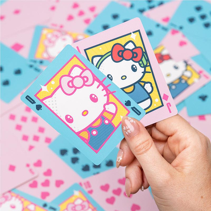 Hand holding Hello Kitty playing cards with pink hearts and blue suit symbols