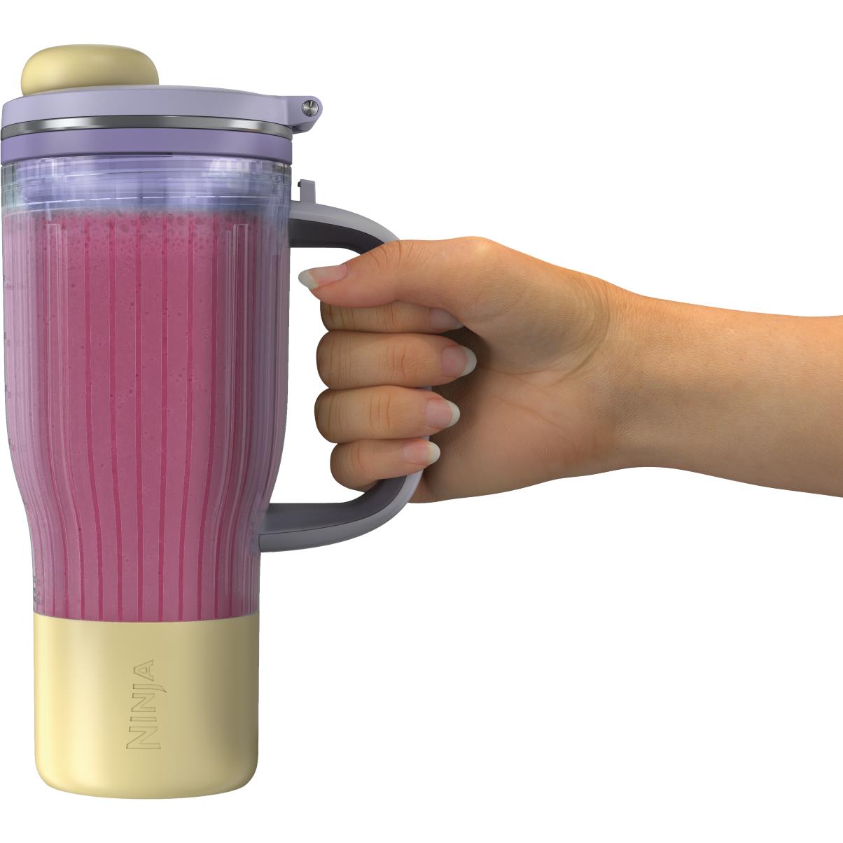 Tumbler blender with clear cup, gold base, and carry handle being held