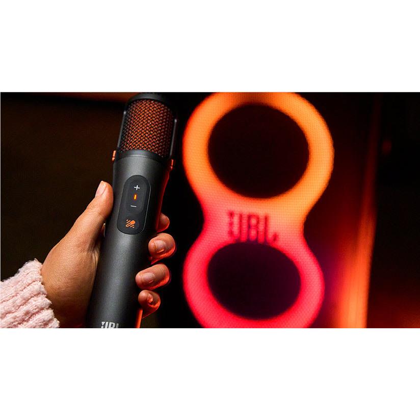 Hand holding a JBL karaoke microphone with orange mesh grille and lit control buttons