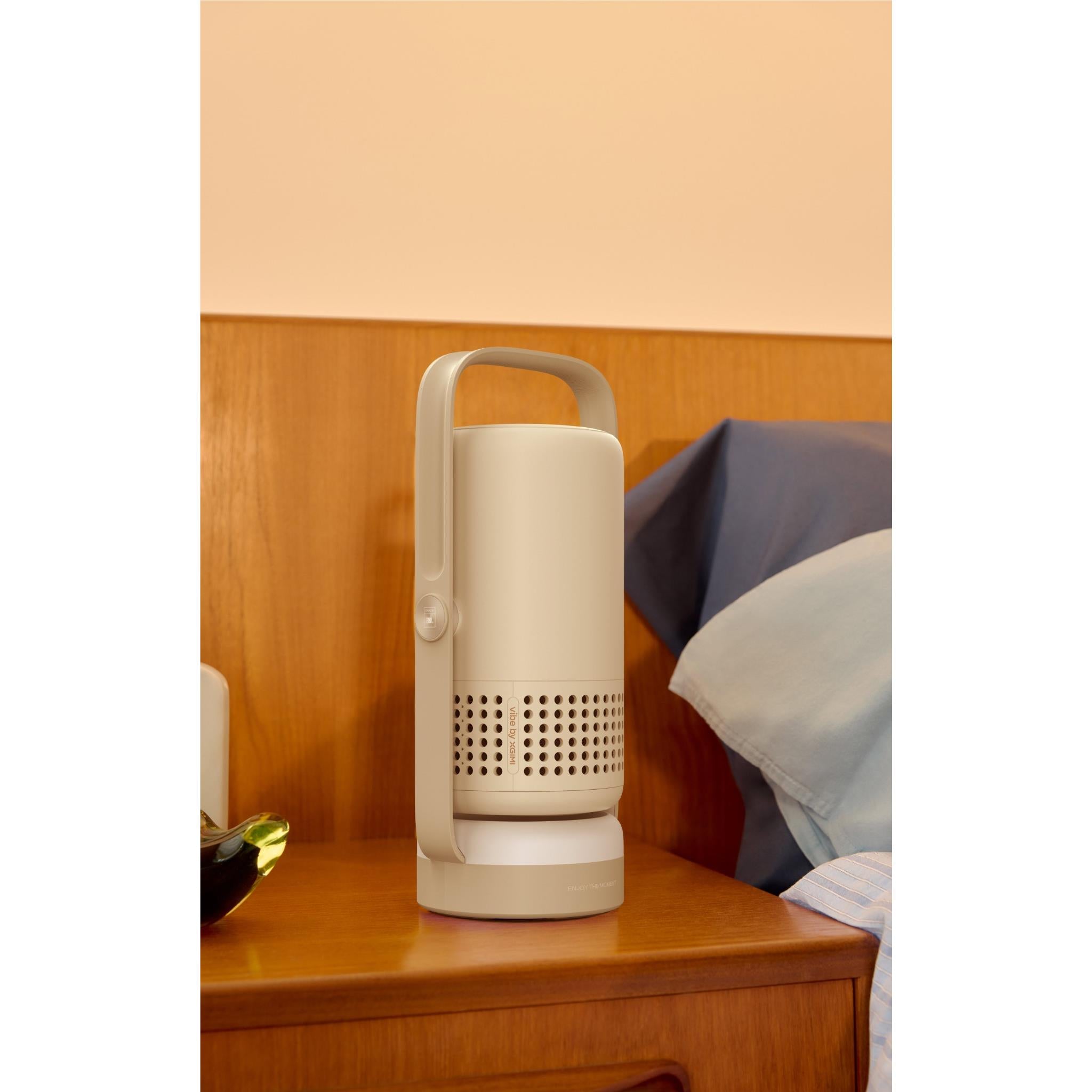 Portable projector standing on a table, front speaker grille, and handle frame; light gray/white.