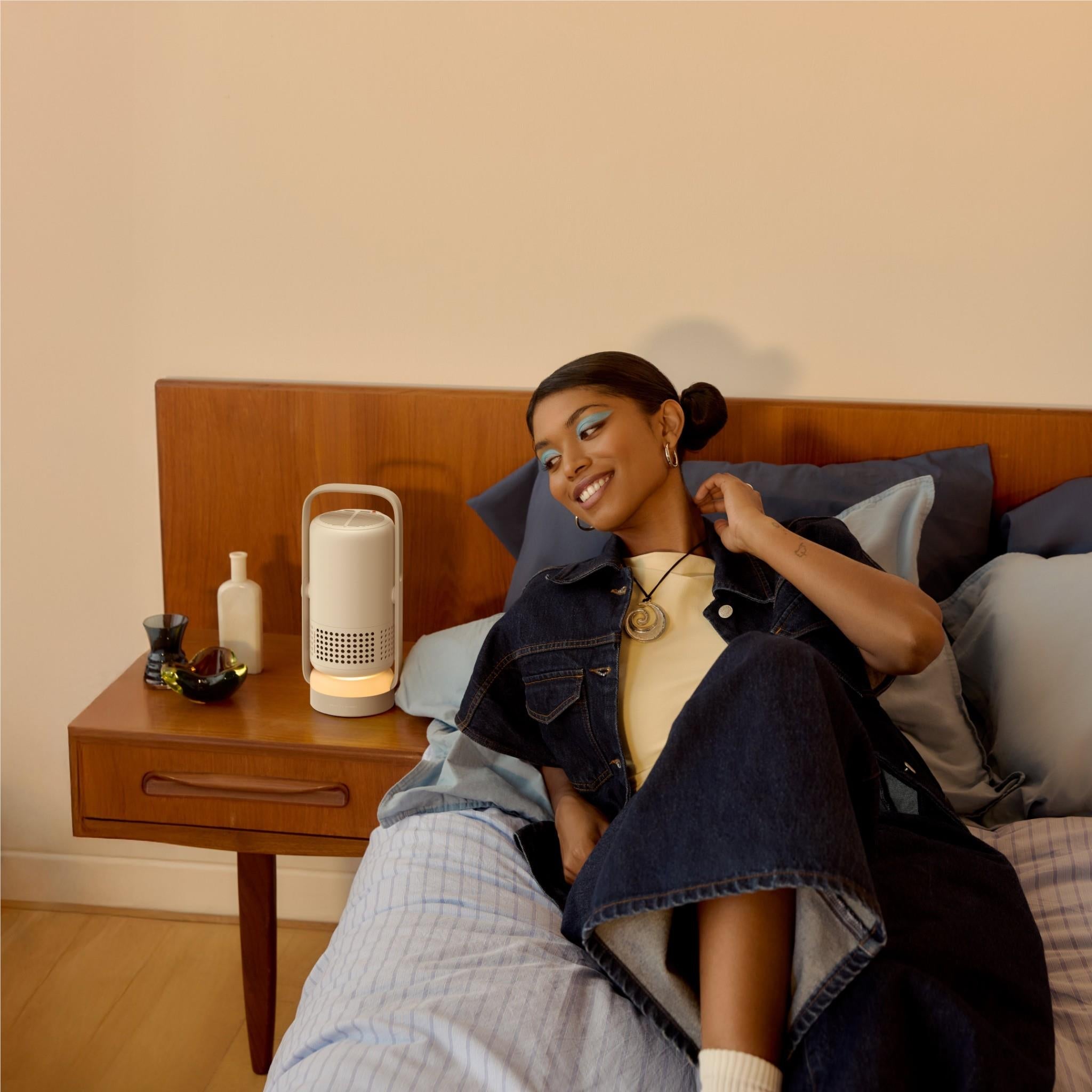 Portable projector on a bedside table, vertical light gray/white body with speaker grille.