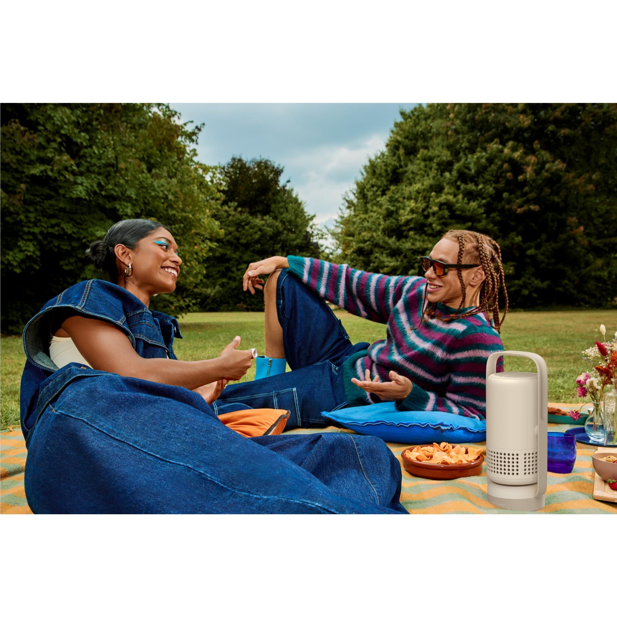 Portable projector on an outdoor picnic table, light gray/white body with handle and grille.