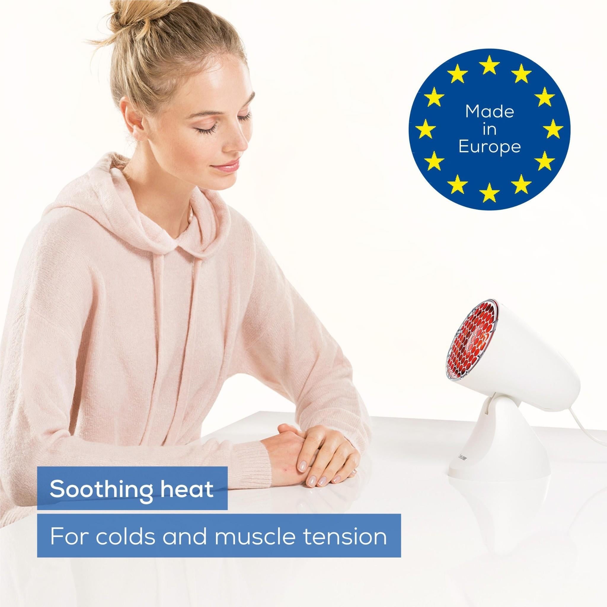 Beurer infrared heat lamp on stand with red protective grille next to seated person
