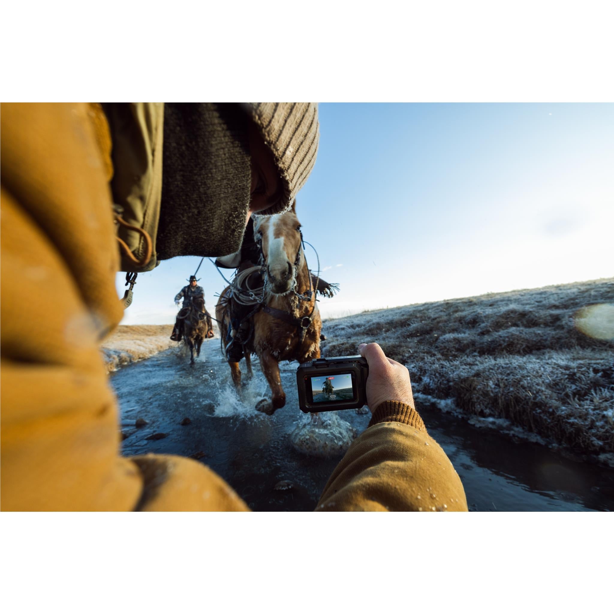 GoPro camera grip with cold shoe mount, held outdoors by a person and horse