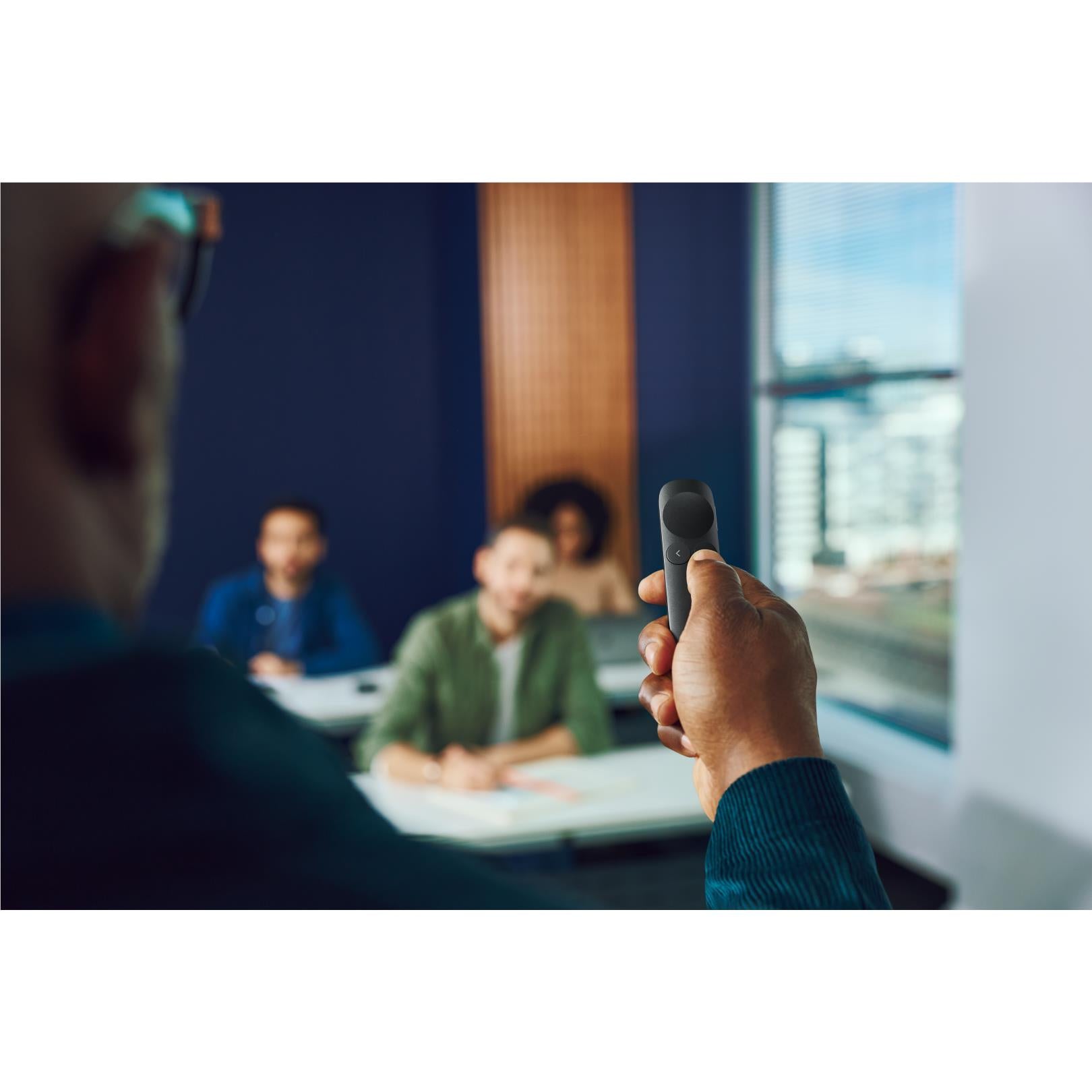 Wireless presentation remote in hand with thumb over top button, dark graphite