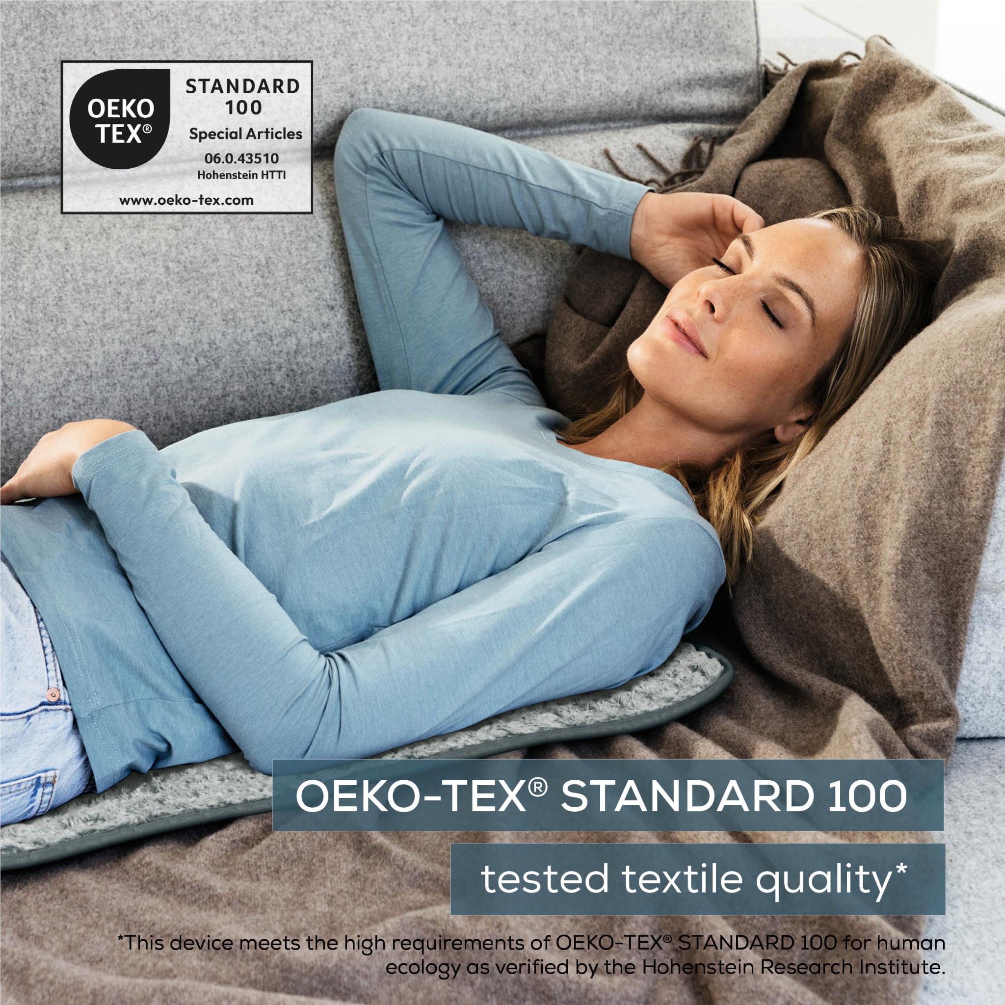 Grey heating pad beside a sleeping person’s legs with controller connected