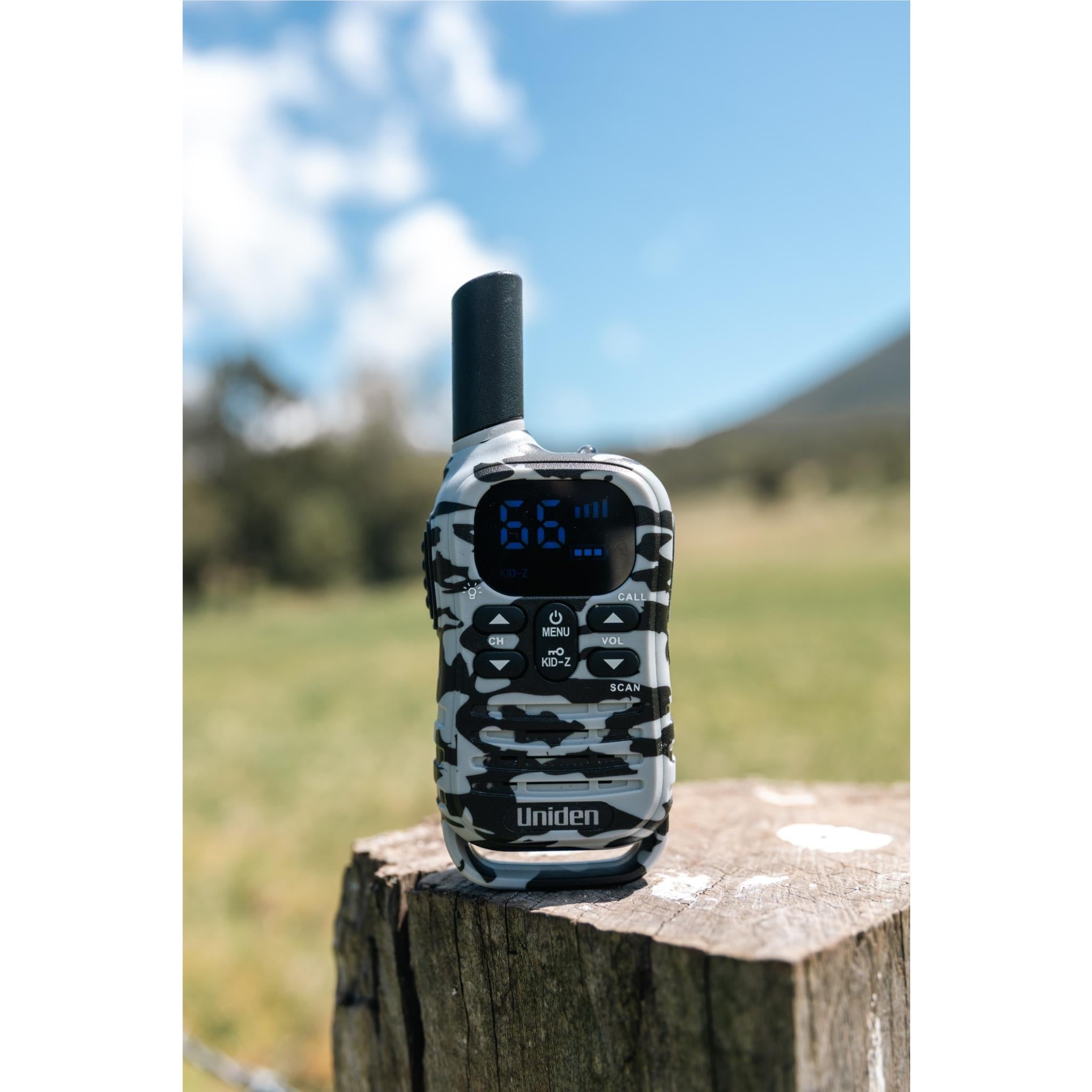 Camouflage UHF kid-zone radio on outdoor surface, blue LCD screen lit