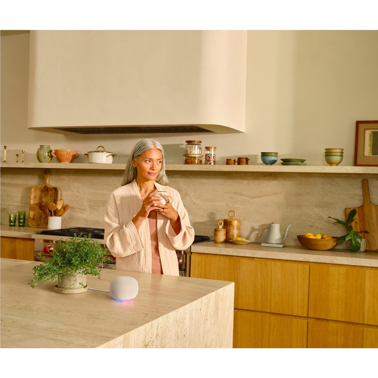 Google Home smart speaker, porcelain white puck on kitchen countertop beside woman