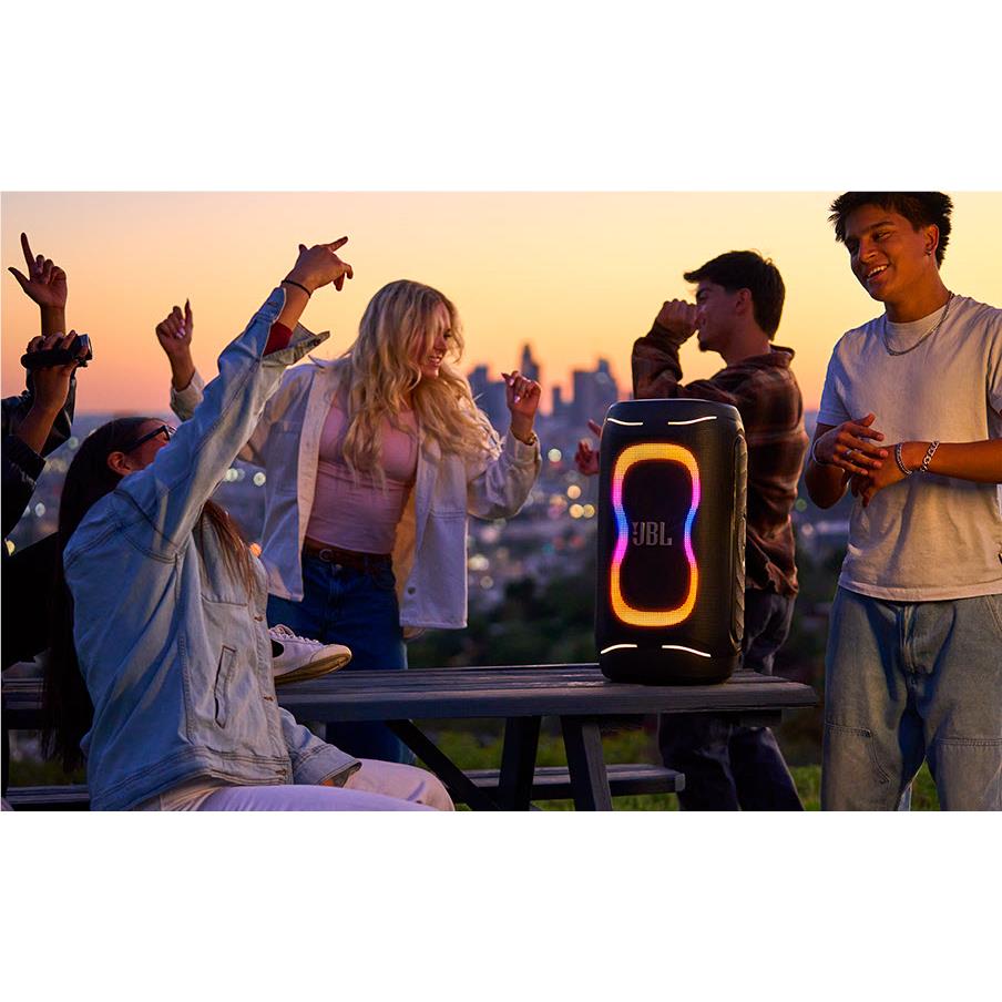 Black portable party speaker with orange LED, on outdoor table during a group gathering