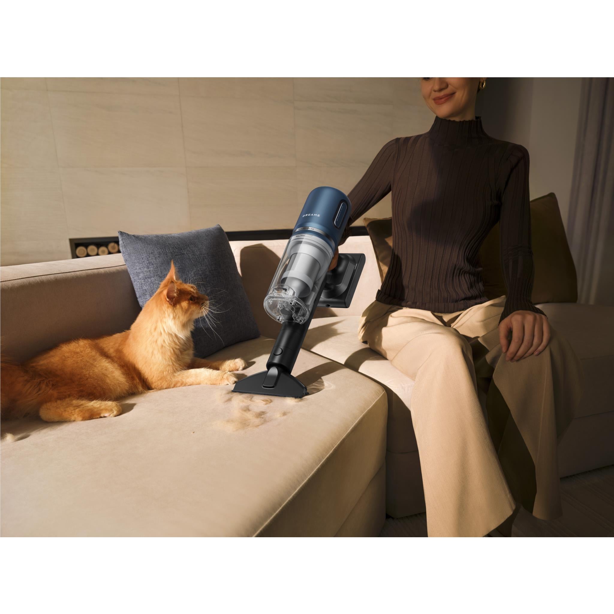 Cordless stick vacuum cleaning a sofa while a cat lies on the cushion