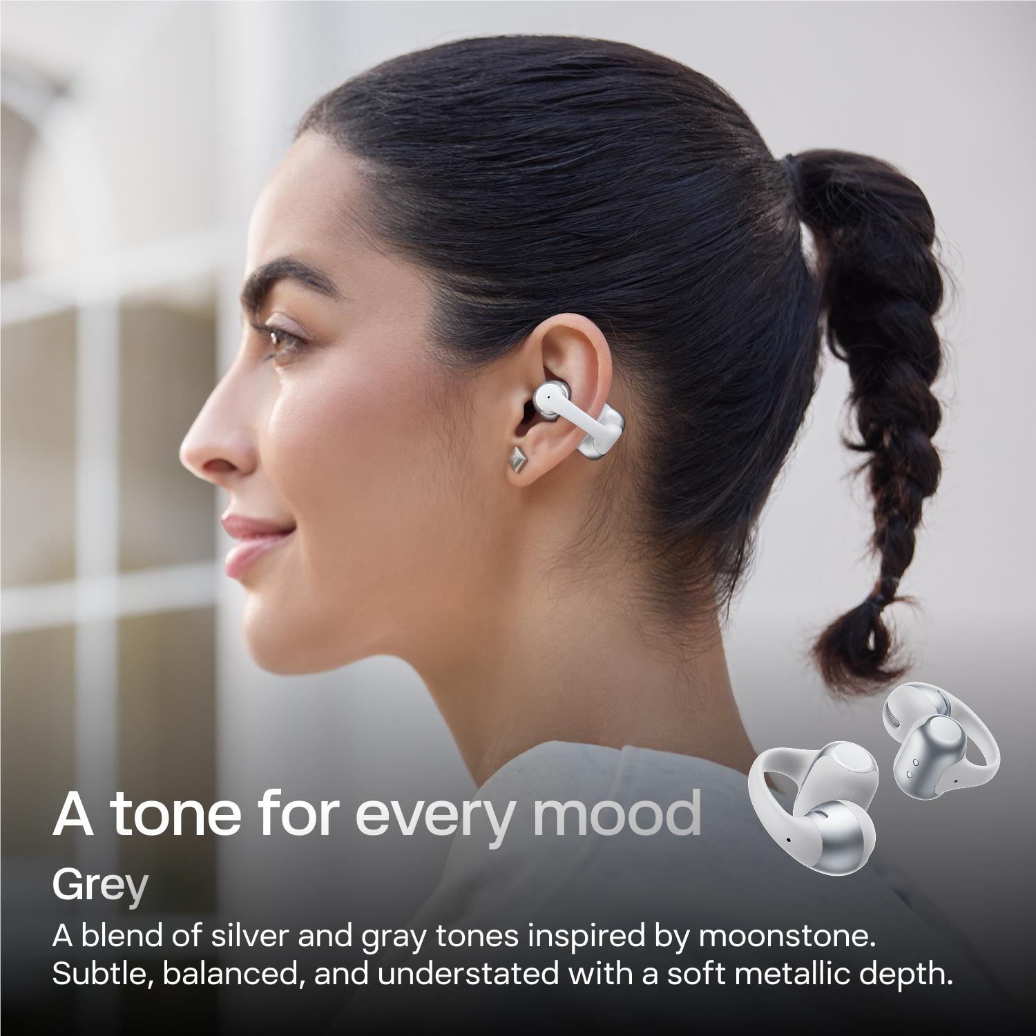 Woman wearing grey open-ear wireless earbuds on her right ear.