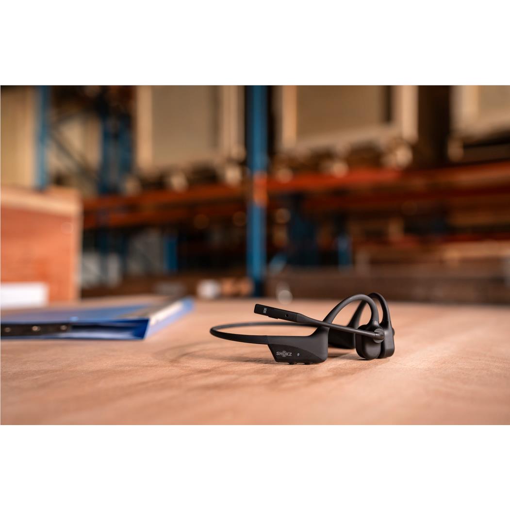 Black open-ear bone conduction headset resting on desk with control module