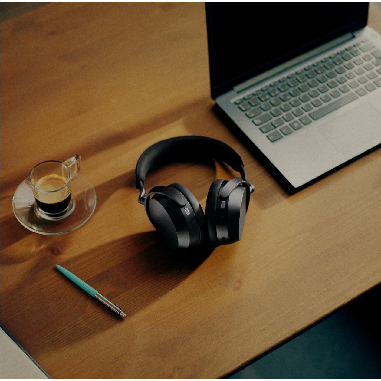 Black over-ear headphones resting on a wooden desk near a laptop