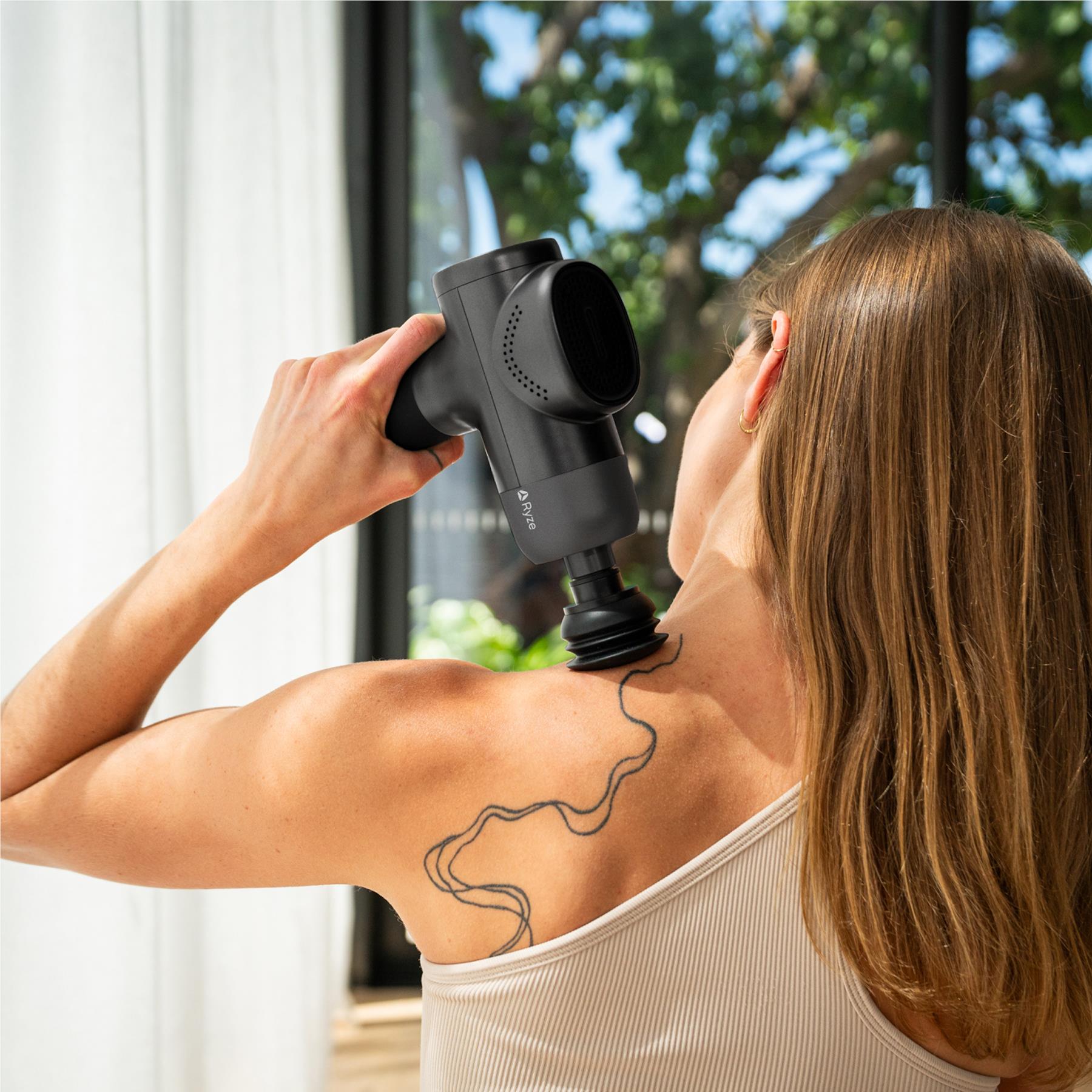 Ryze massage gun used on a person’s shoulder with round massage head