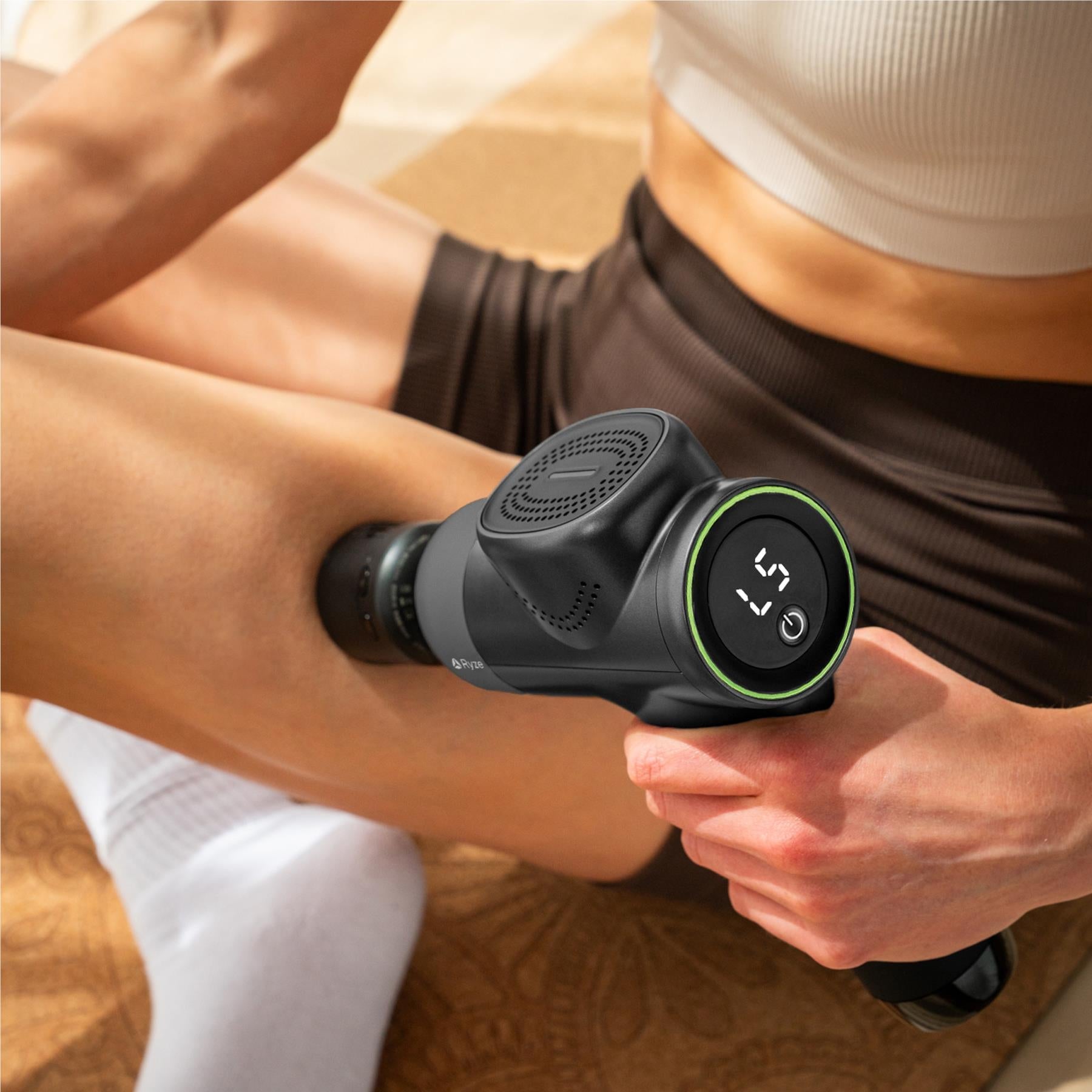 Ryze massage gun in use on a person’s leg with rounded massage head