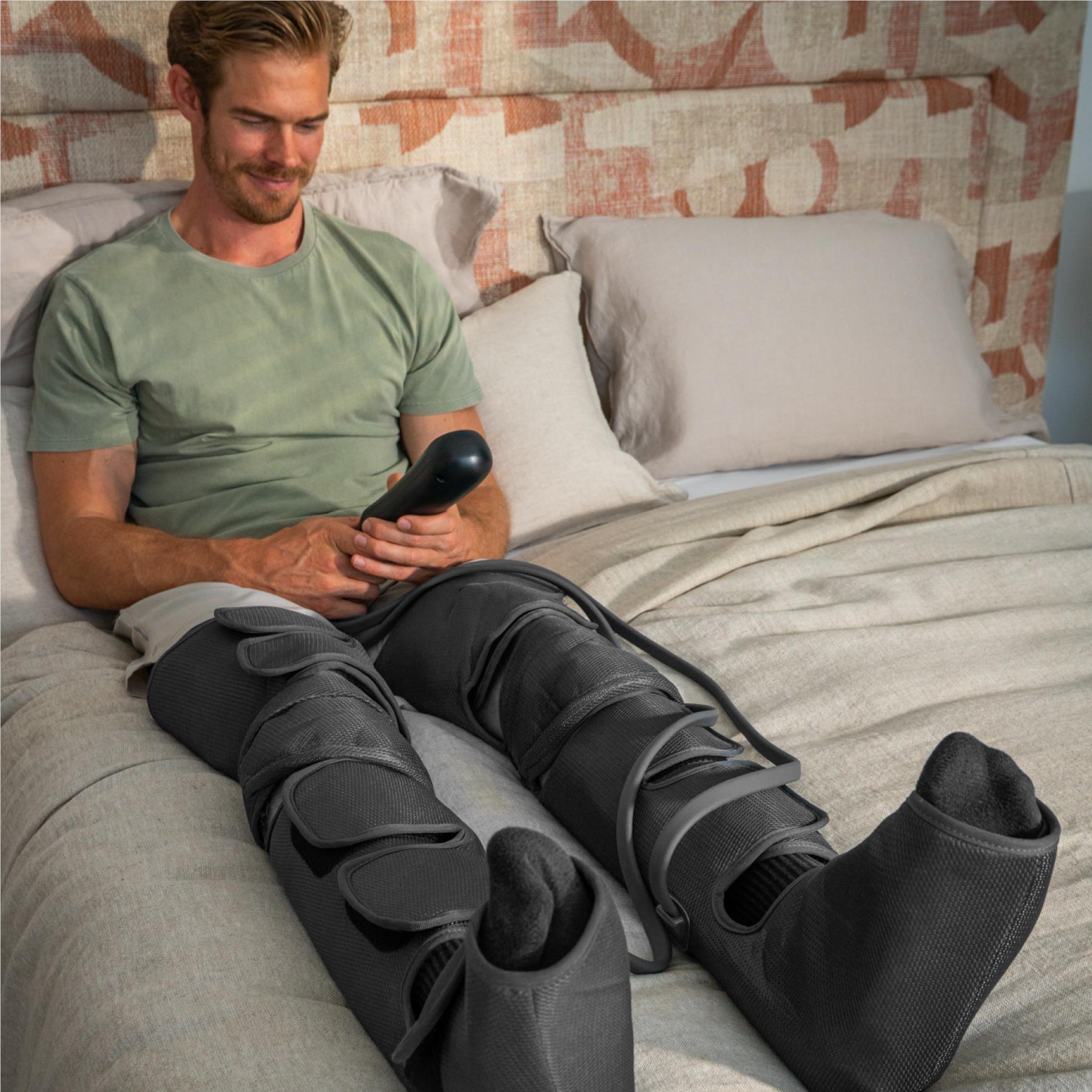 Man using dark gray leg compression massager on a sofa with heated sleeve fit