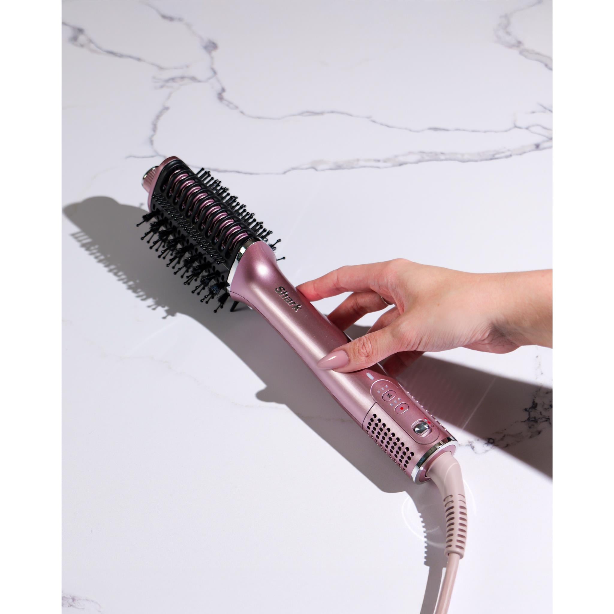 Pink hot air hair styler in hand with round brush head styling hair