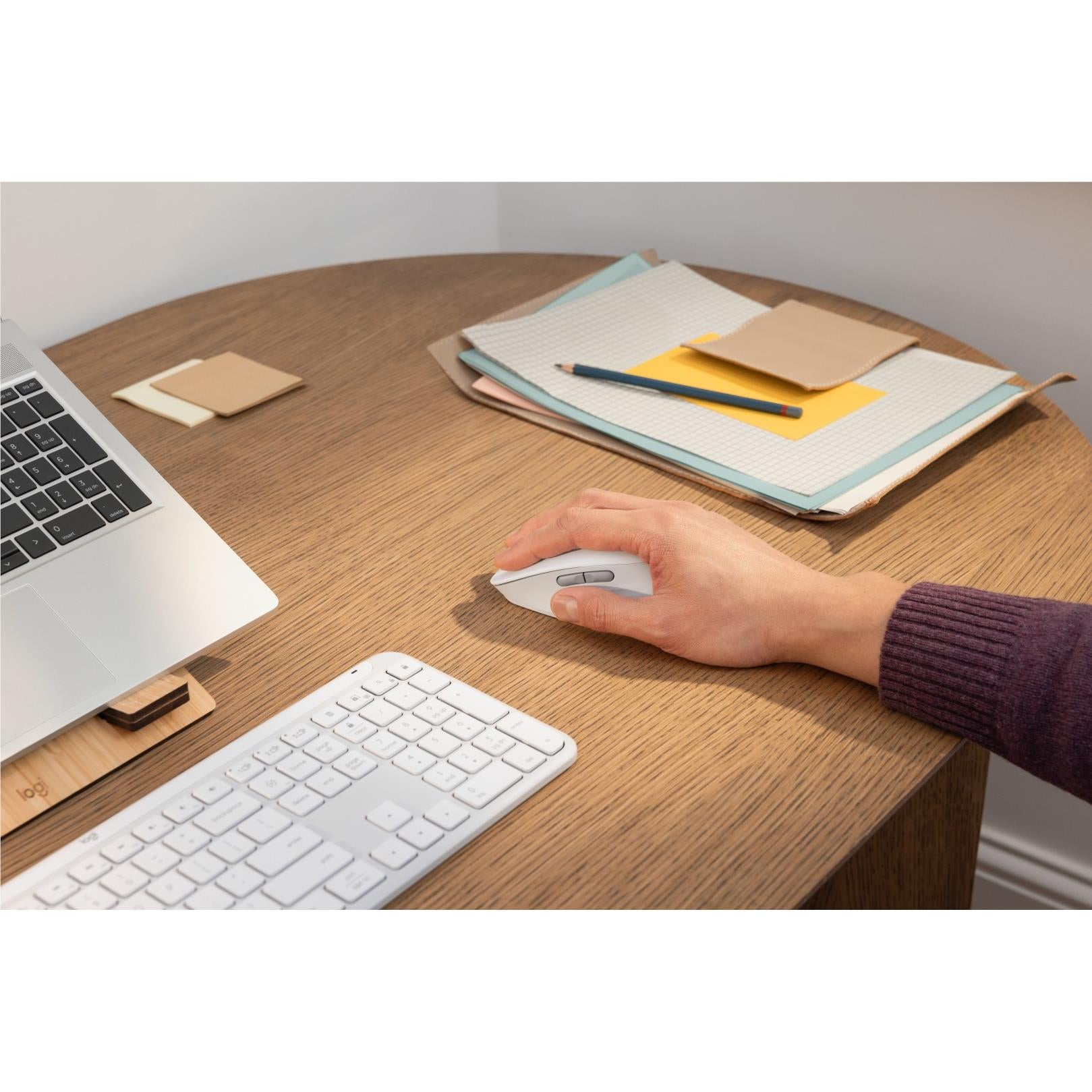 Off-white Logitech mouse in hand on desk, with keyboard and stationery nearby