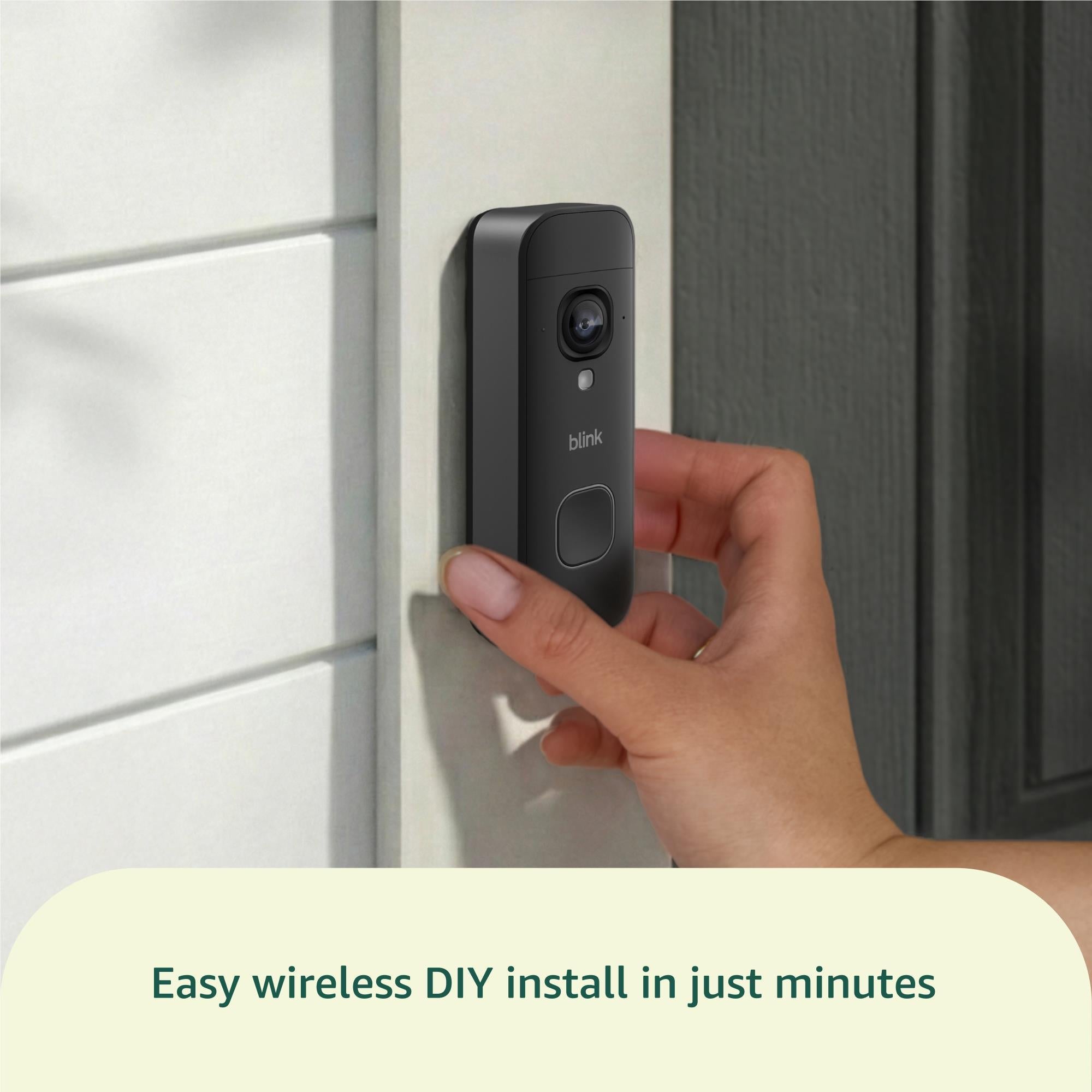 Black wire-free video doorbell being attached by hand to an exterior wall