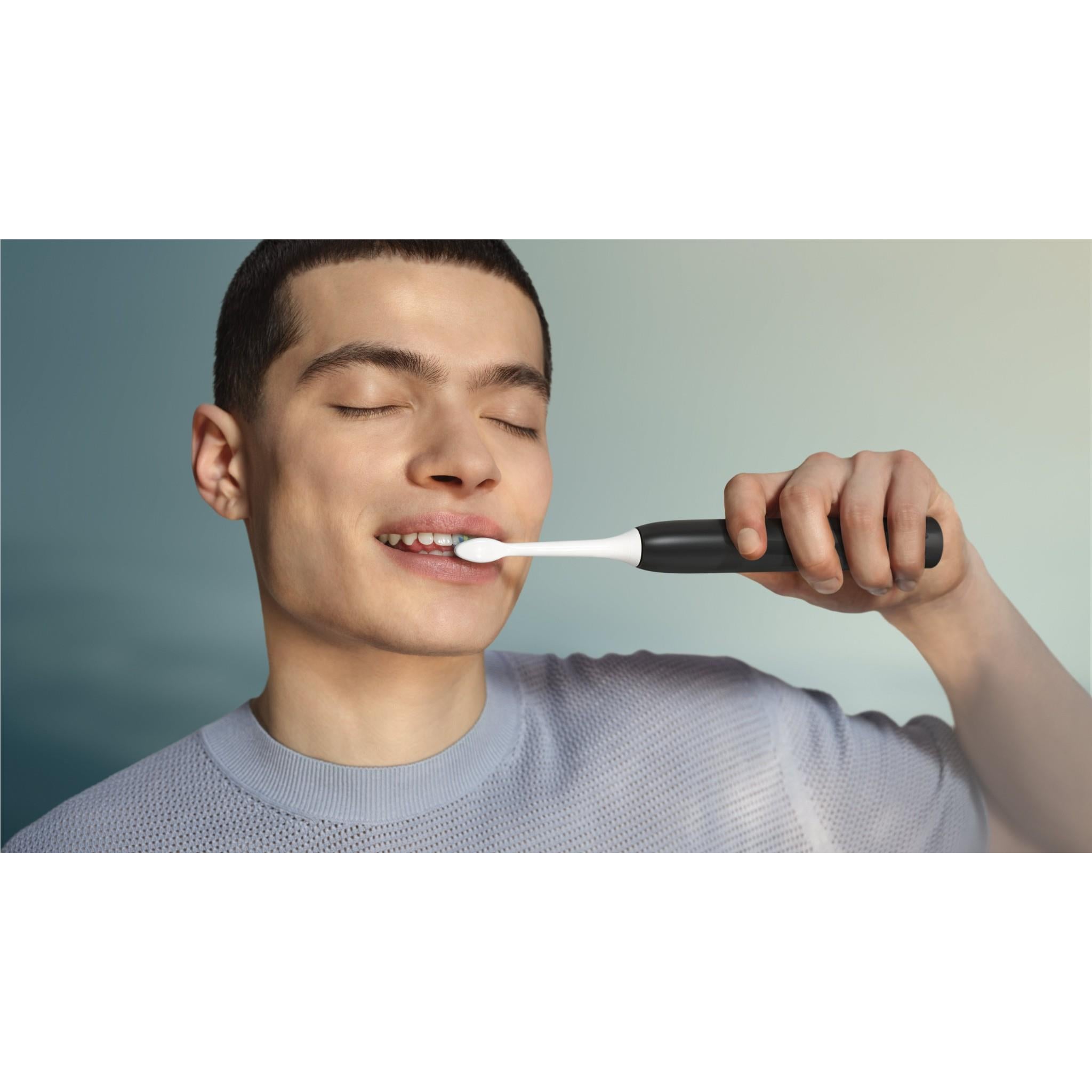 Black electric toothbrush held in hand, bristles touching teeth