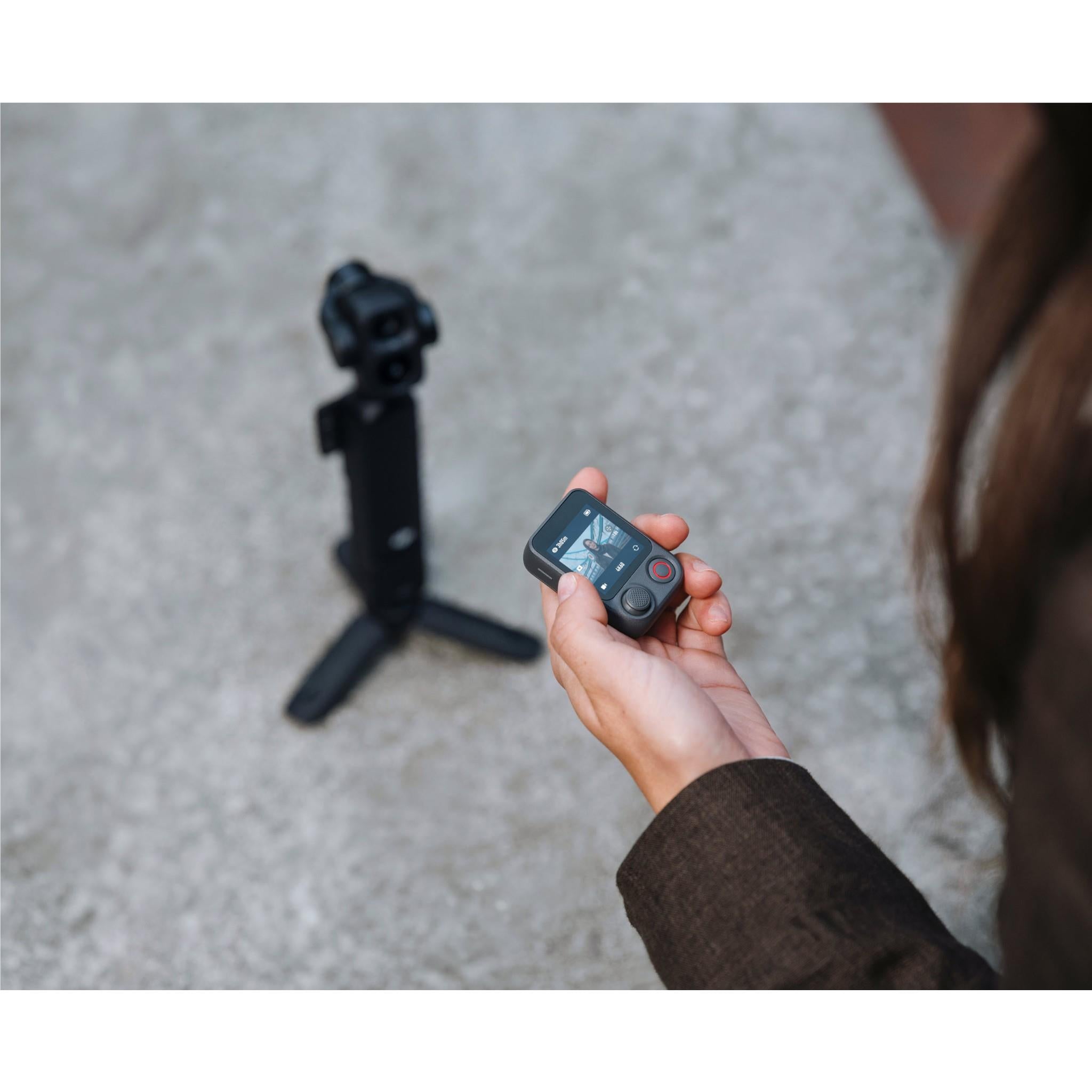 Black gimbal camera being held, with dual-lens head and mini tripod nearby