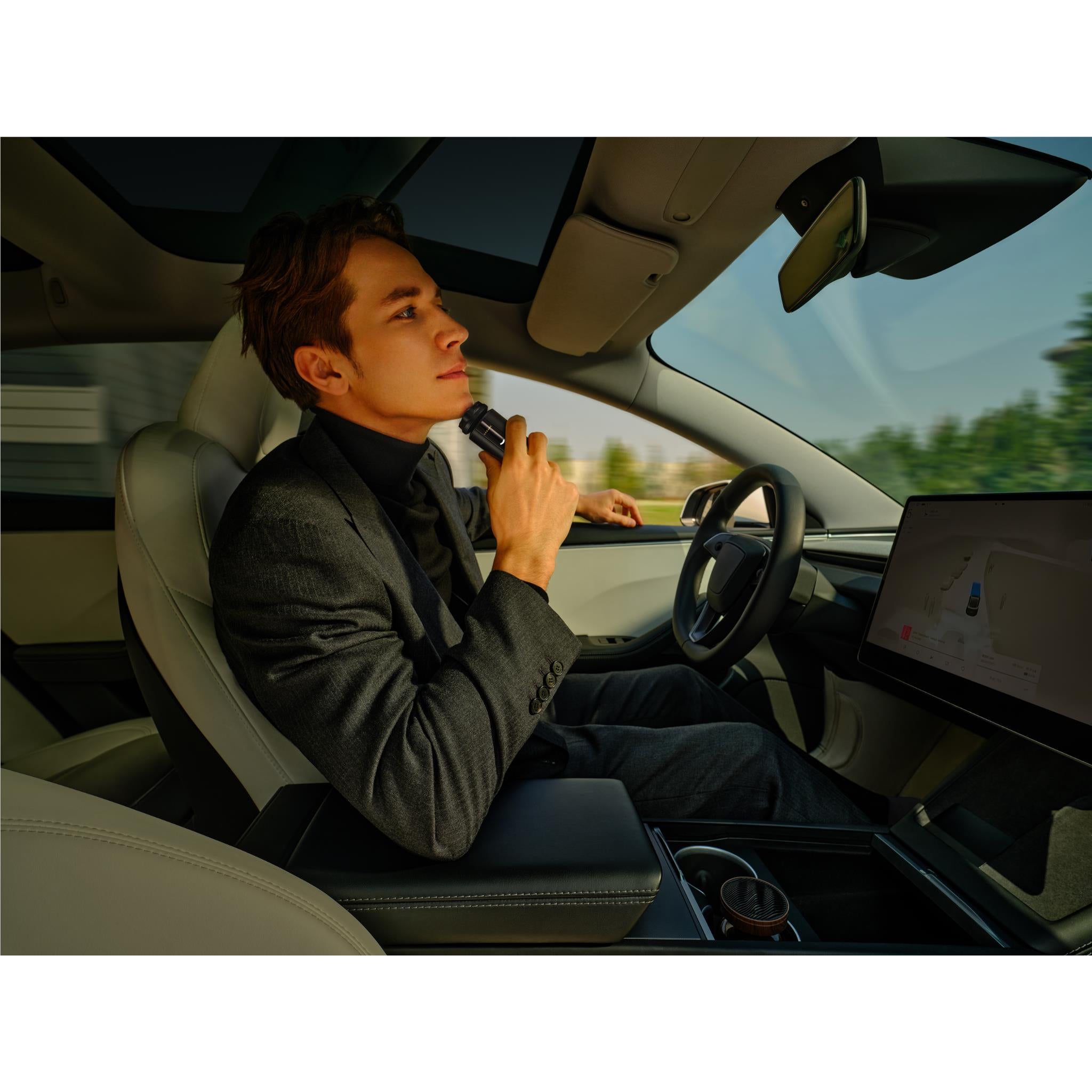 Man shaving in a car holding a black electric beard shaver to his cheek