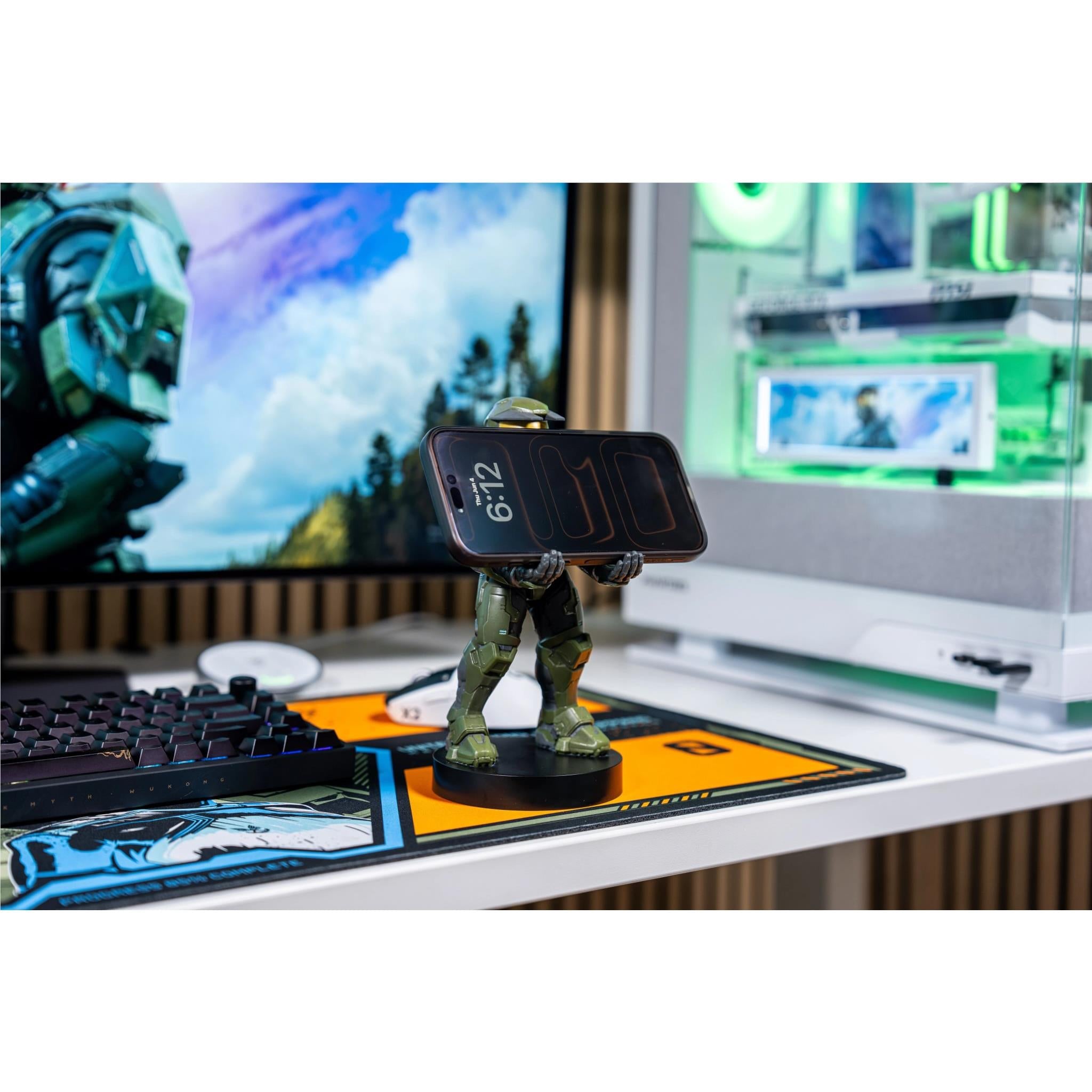 Green armored figure phone stand on desk holding a dark smartphone, black round base