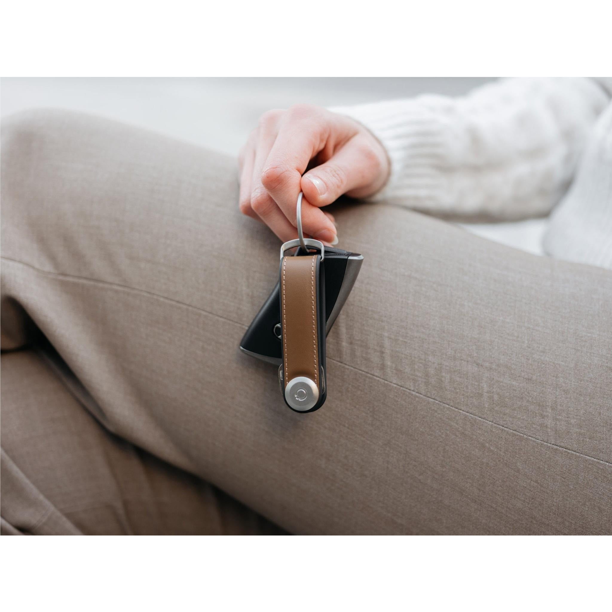 Brown leather key holder clipped in hand with small round locking cap.