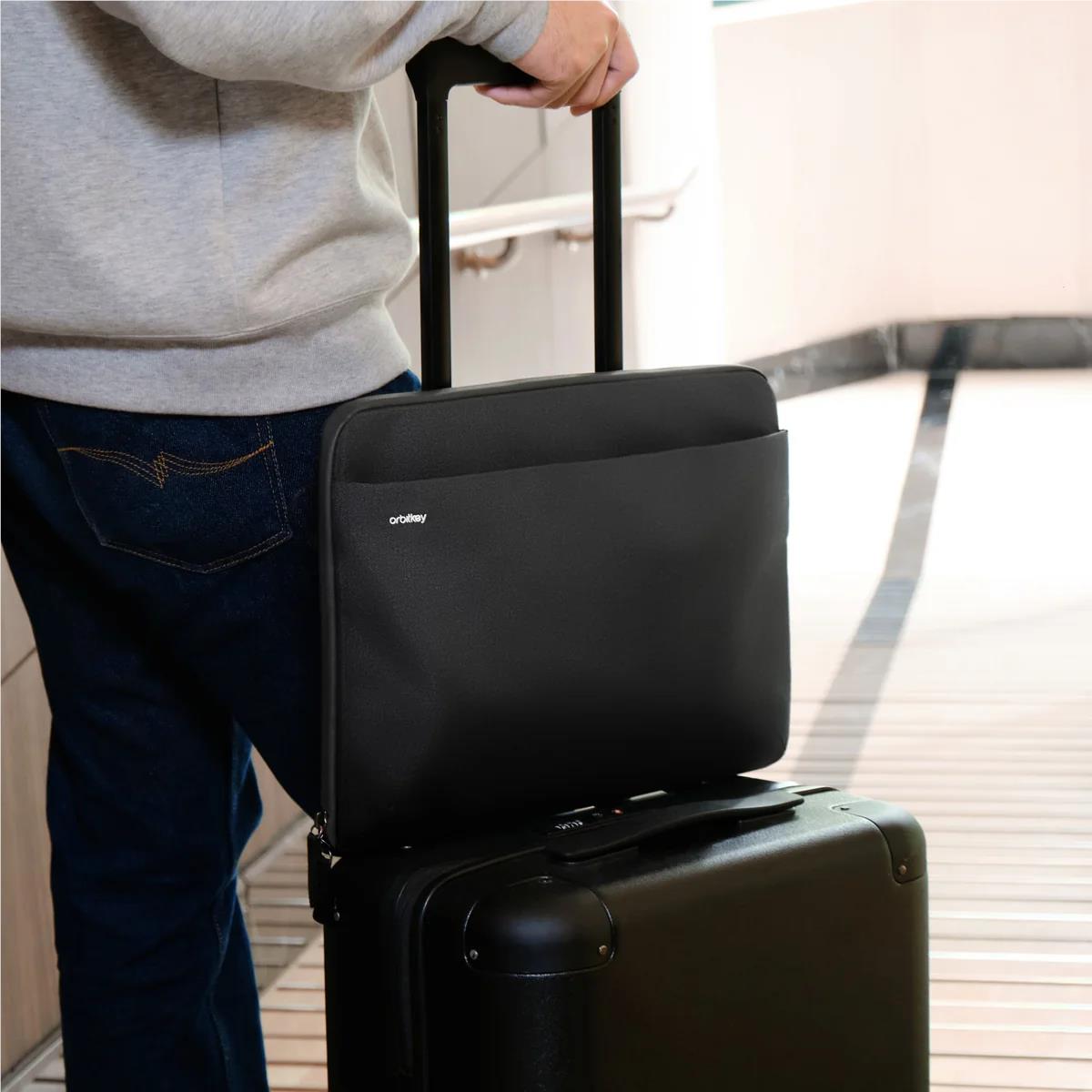 Black laptop sleeve resting on a rolling suitcase handle