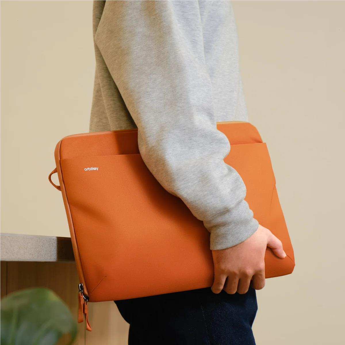 Terracotta laptop sleeve carried by hand with zip closure and side pull tab
