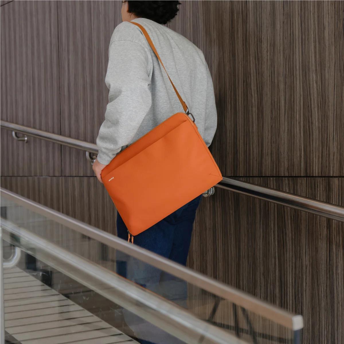 Terracotta messenger-style laptop sleeve with shoulder strap worn crossbody