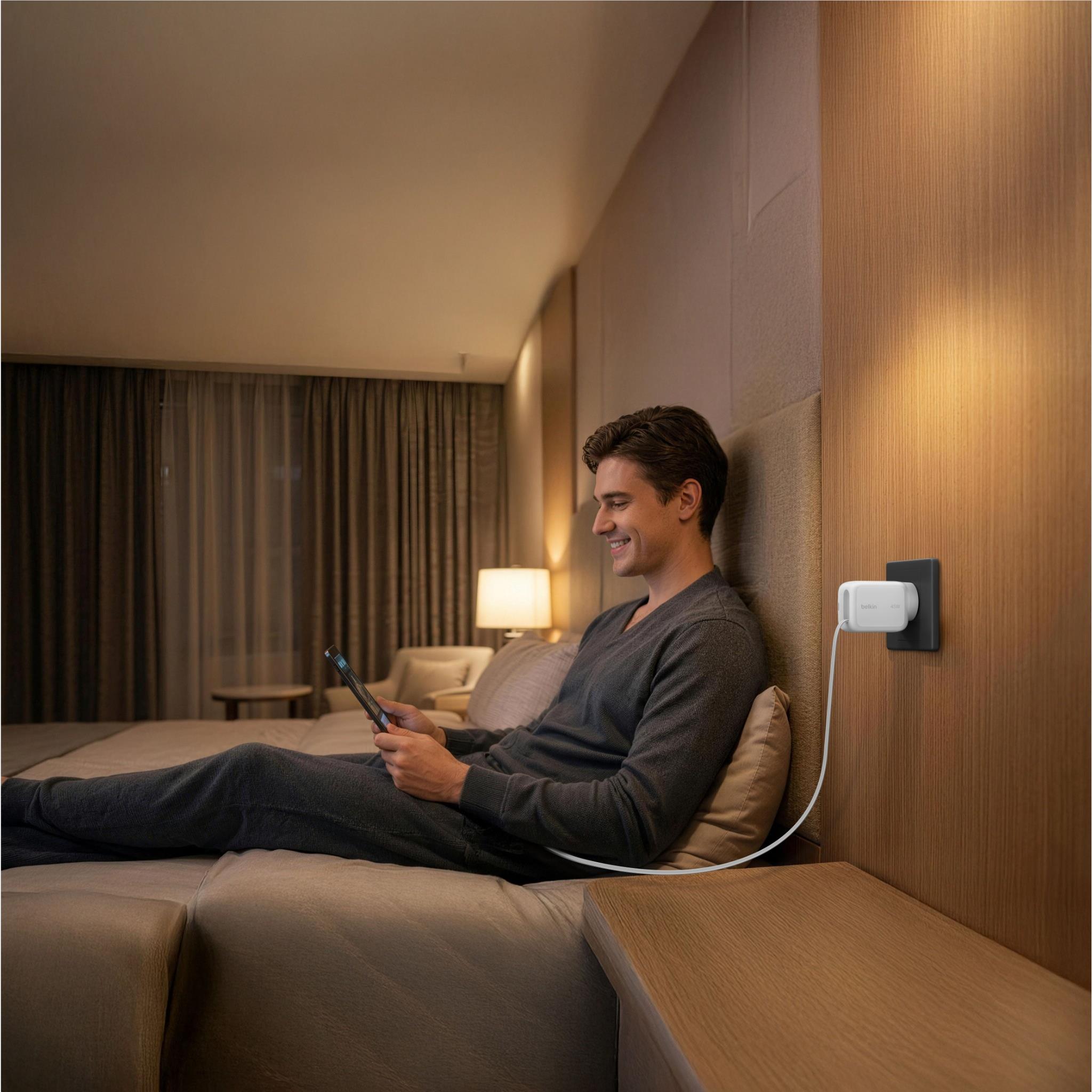 White wall charger mounted beside bed with USB-C cable charging a phone
