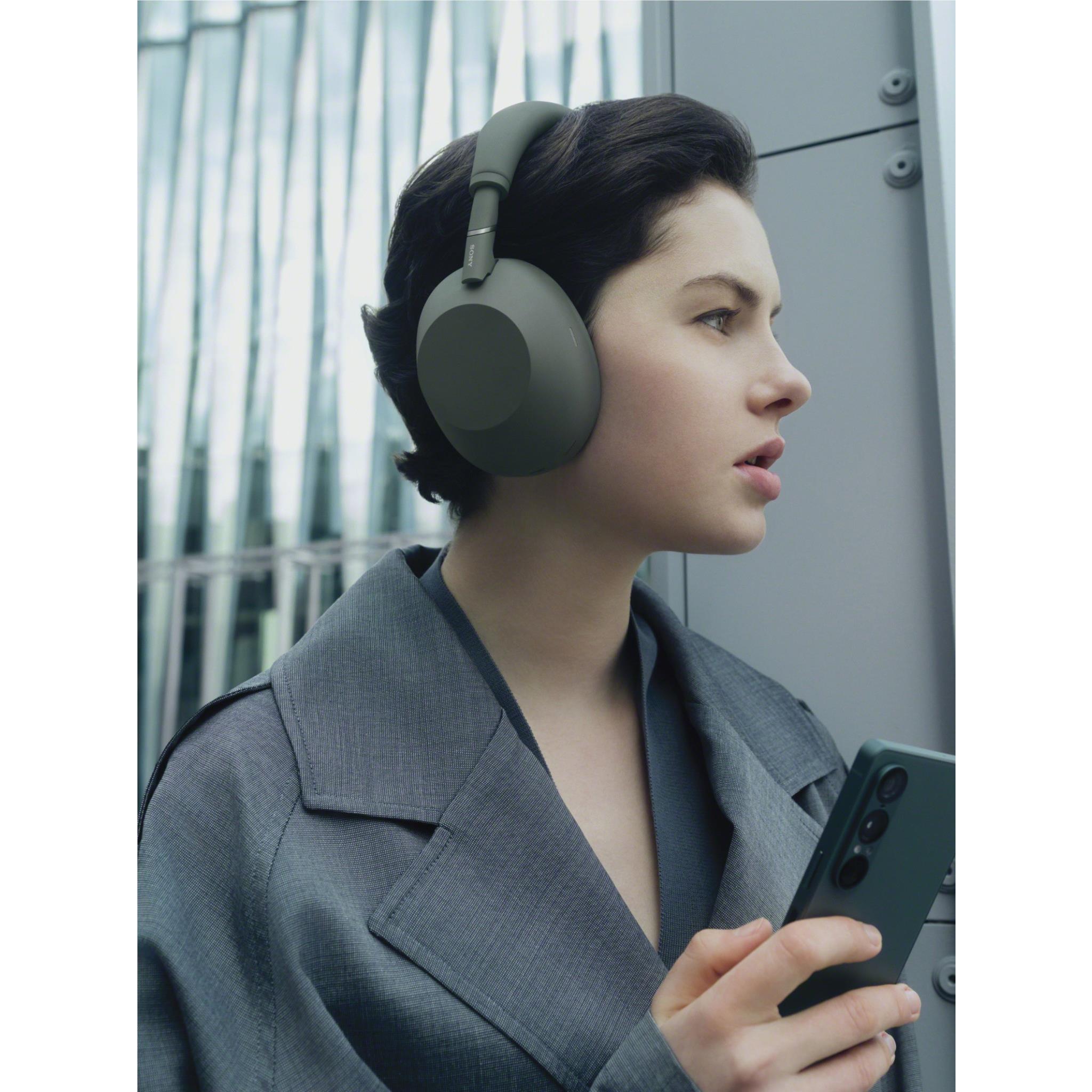 Olive grey over-ear headphones on a person wearing the headset while holding a phone.