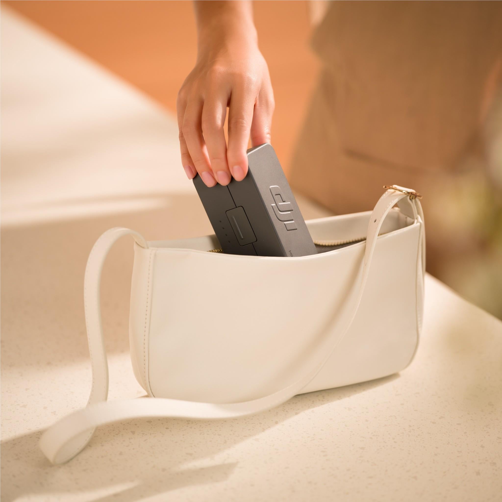 White crossbody bag holding a black DJI wireless microphone receiver unit