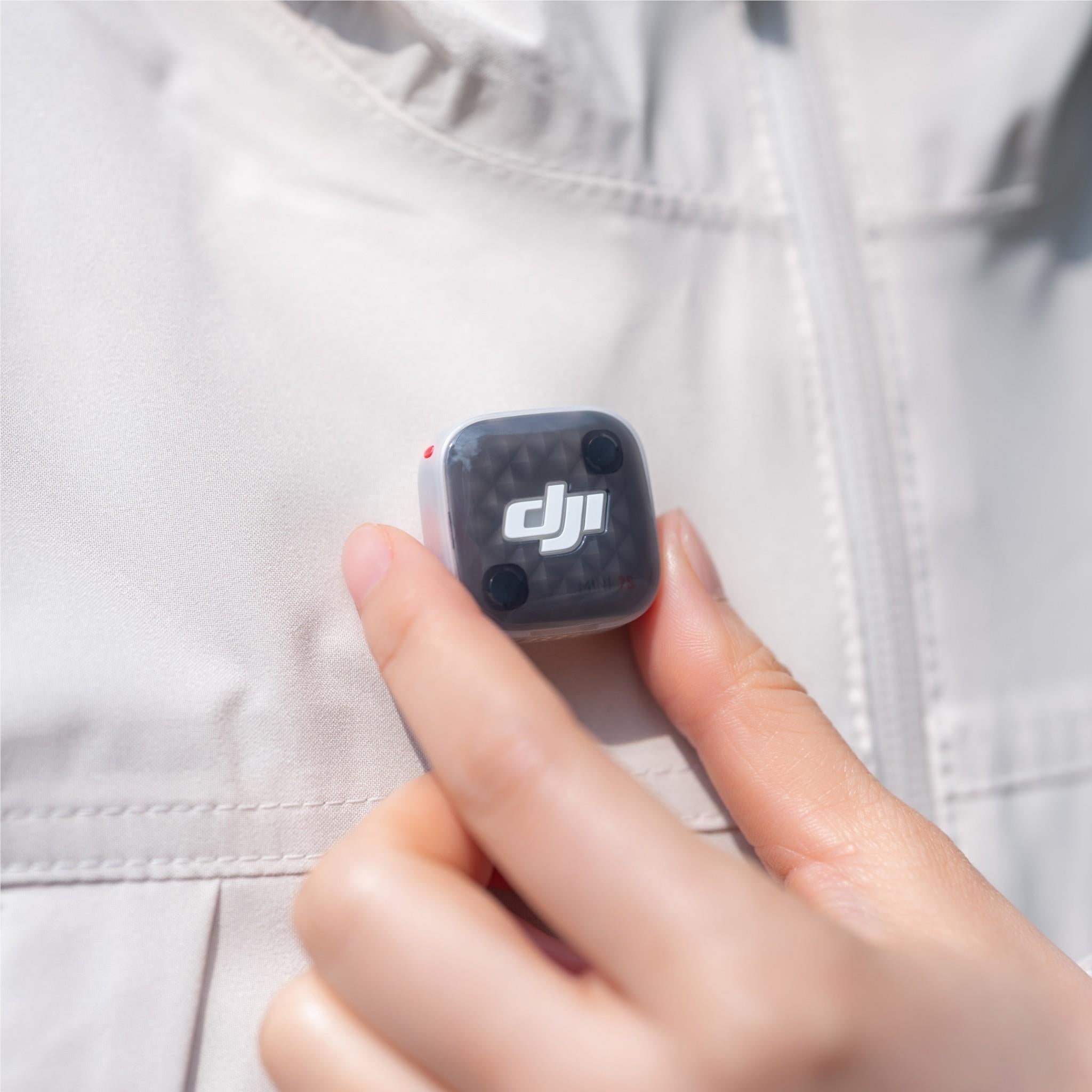 Person holding a small blue DJI wireless transmitter against a white shirt
